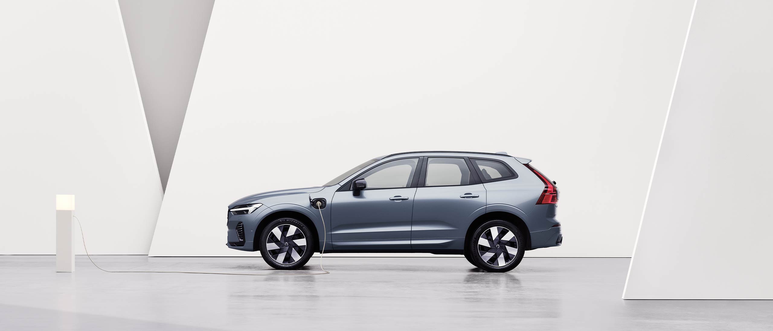 A gray Volvo XC60 Recharge, charging in a white surrounding.