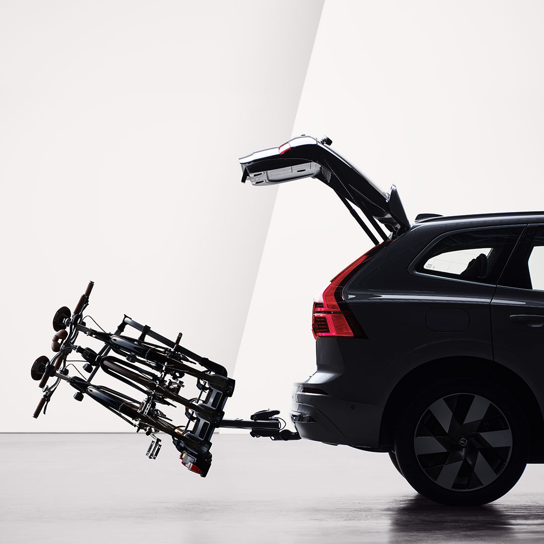 An open tailgate and a bicycle holder attached by tow bar folded down on the rear of a Volvo XC60 Recharge.