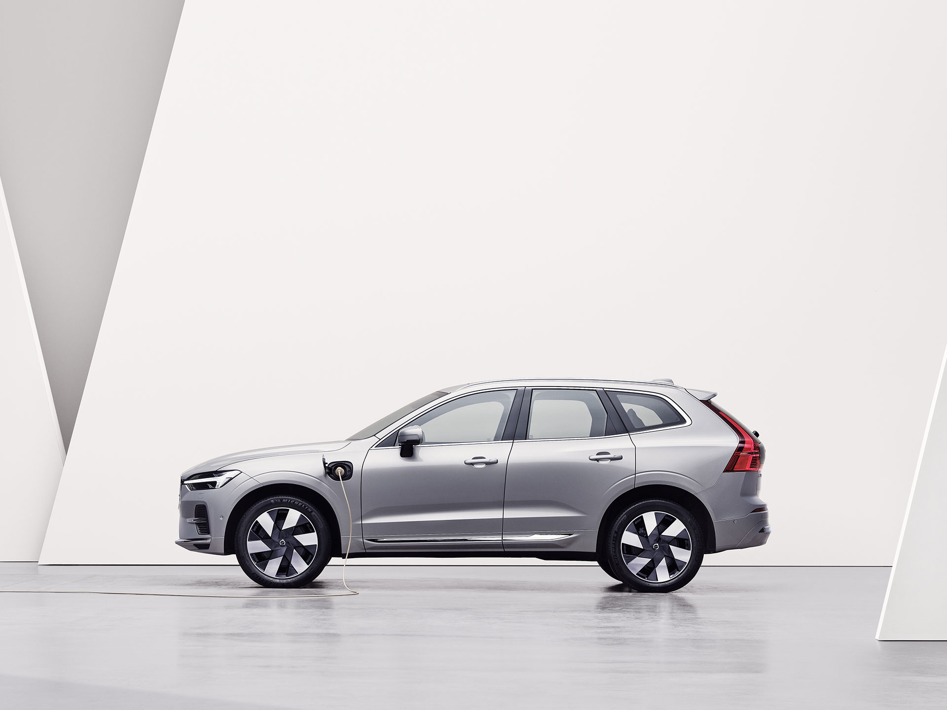 A silver Volvo XC60 Recharge, charging in a white surrounding.