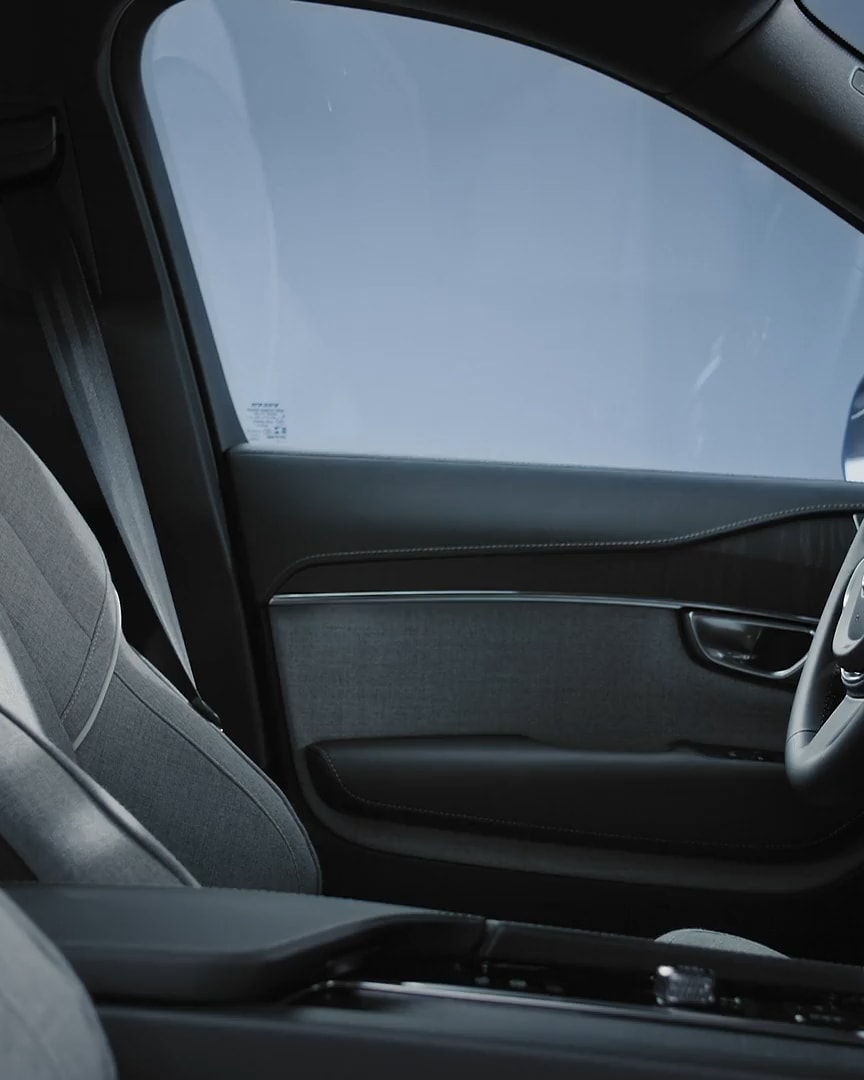 Passenger view of the Volvo XC90 Recharge plug-in hybrid driver’s seat and door in available wool upholstery and black steering wheel.