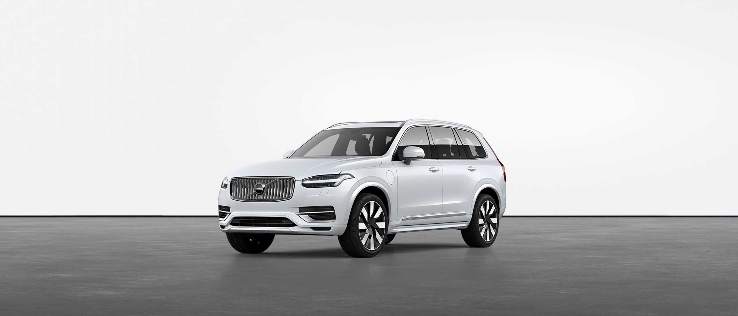 Ein weisser Volvo XC90 Recharge Plug-in Hybrid SUV steht auf einem grauen Boden in einem Studio.