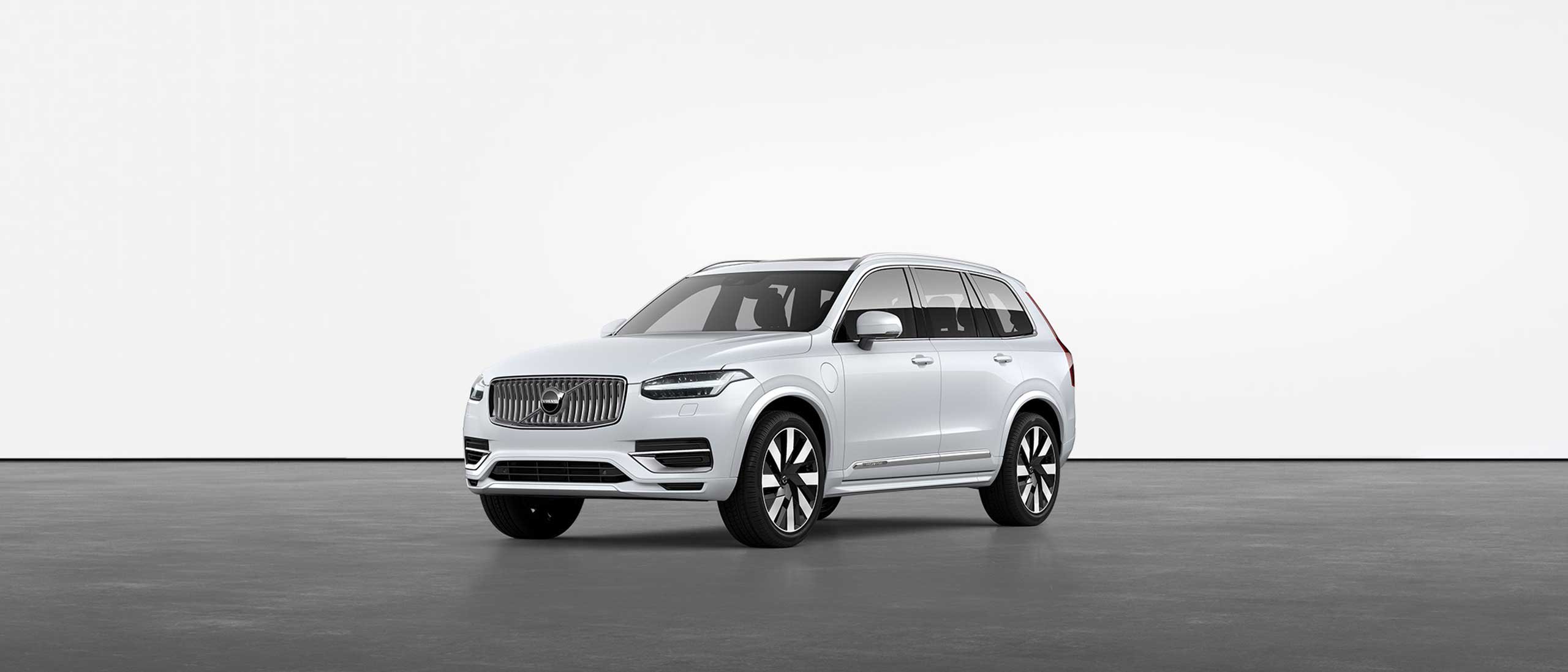 Valkoinen Volvo XC90 Recharge -lataushybridi-SUV paikallaan studiossa harmaalla lattialla.