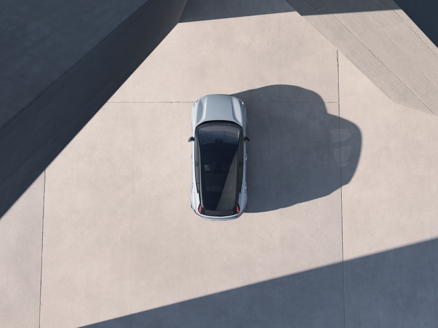 A bird's eye view of a Volvo EX30 that's lit boldly from the side, so it casts a long shadow.