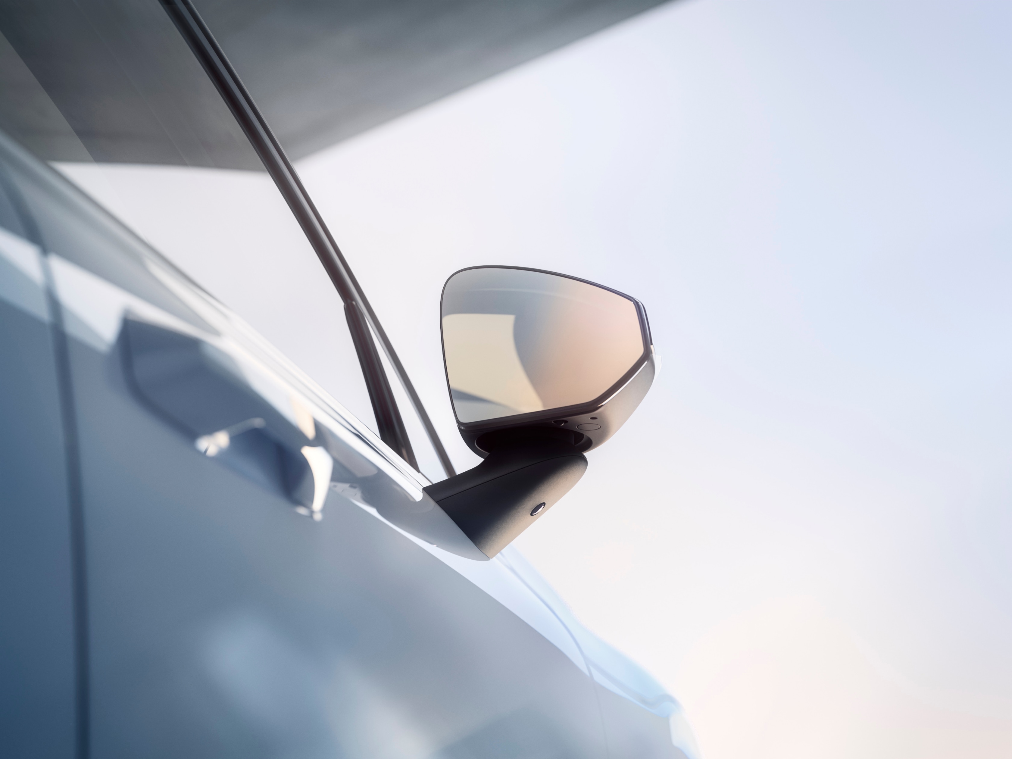 Vonkajšie zrkadlo bez rámčeka vozidla Volvo EX30 na strane spolujazdca lesknúce sa v jasnom slnečnom svetle.