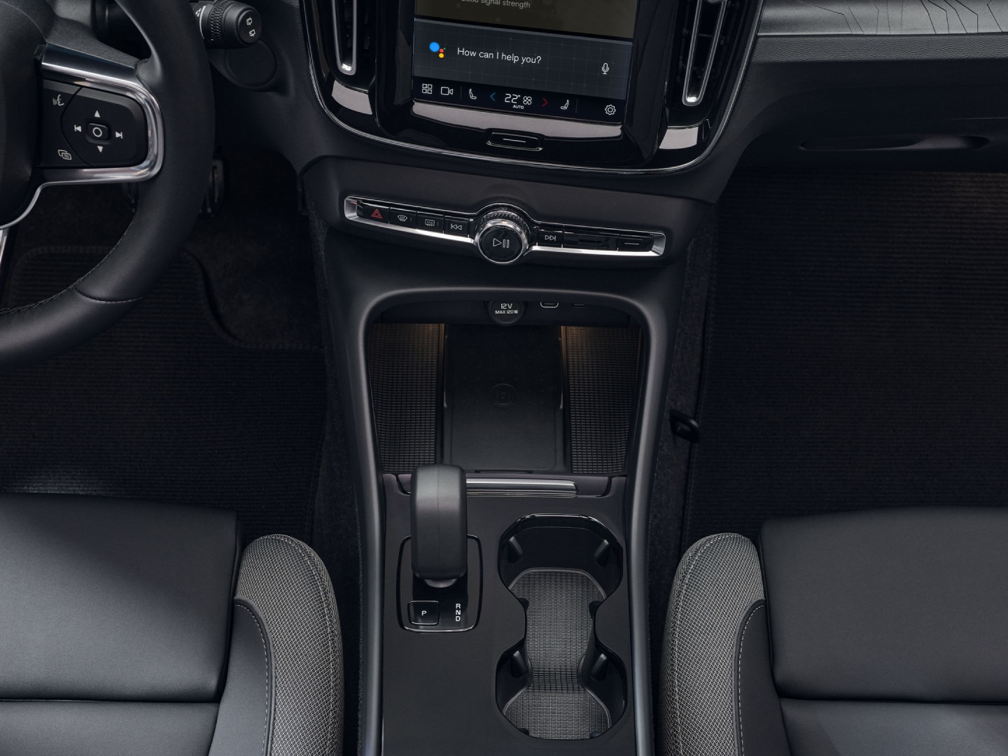 O suporte para copos, a alavanca de velocidades e o carregador sem fios posicionados entre os bancos dianteiros do Volvo EX40 100% elétrico.