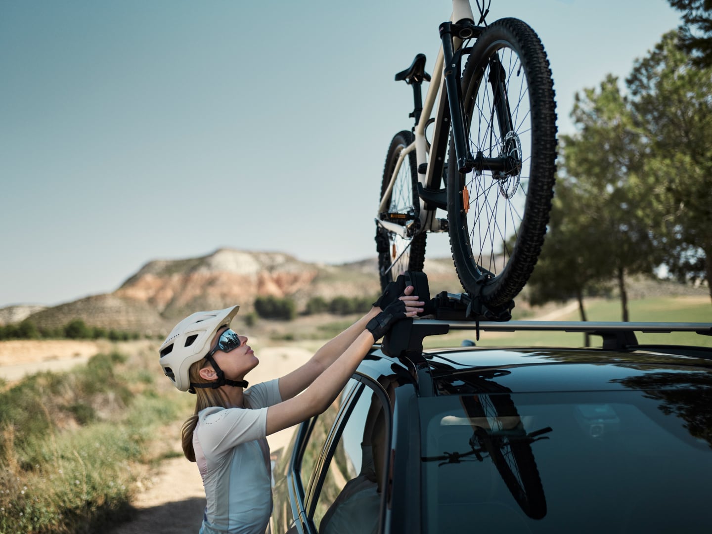 A female cyclist adjusts the position of a bicycle mounted on a Volvo car.
