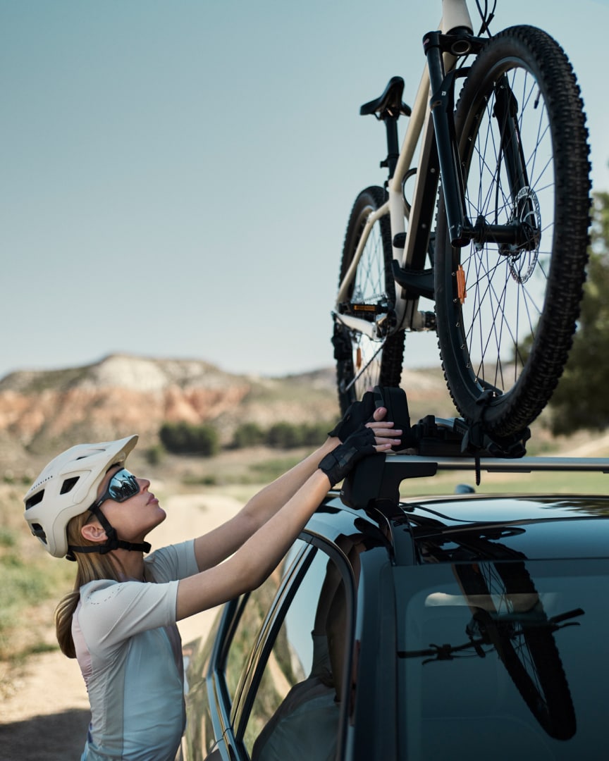 A female cyclist adjusts the position of a bicycle mounted on a Volvo car.