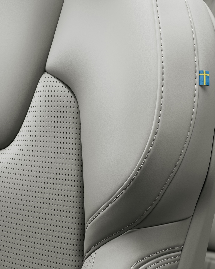 Close-up van het stiksel op de nappalederen passagiersstoel voorin van de Volvo V60 mild hybrid, met een klein Zweeds vlaggetje.