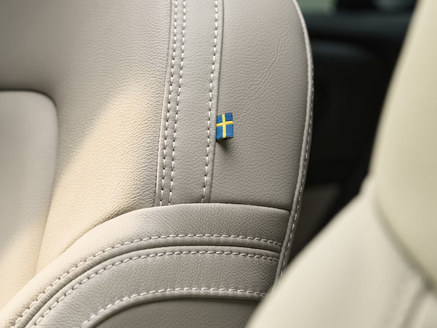 Prim-plan al cusăturilor de pe scaunul din piele al pasagerului din față al Volvo XC40 mild hybrid, cu un mic steag suedez.