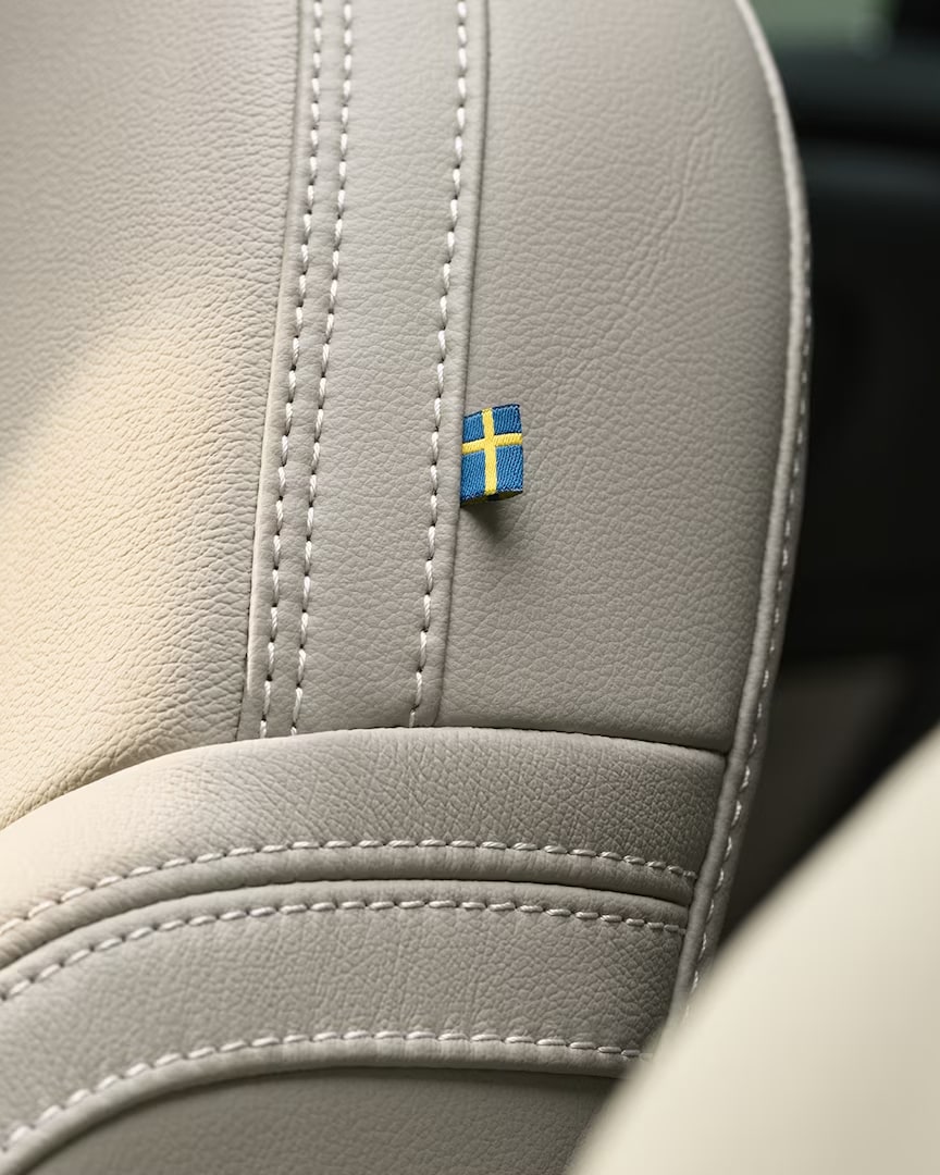 Prim-plan al cusăturilor de pe scaunul din piele al pasagerului din față al Volvo XC40 mild hybrid, cu un mic steag suedez.
