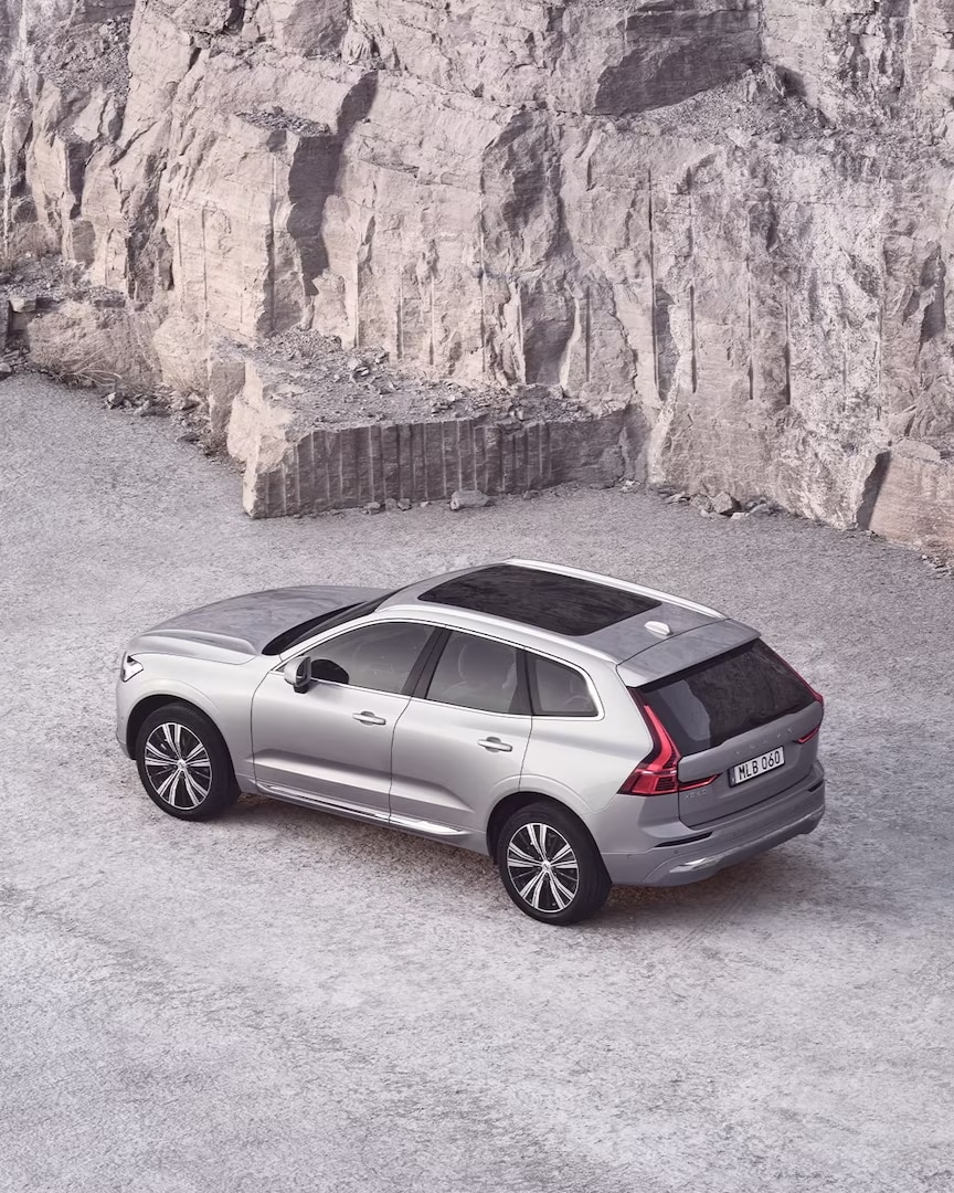 Une Volvo XC60 avec un toit panoramique à côté d’un mur de pierre.