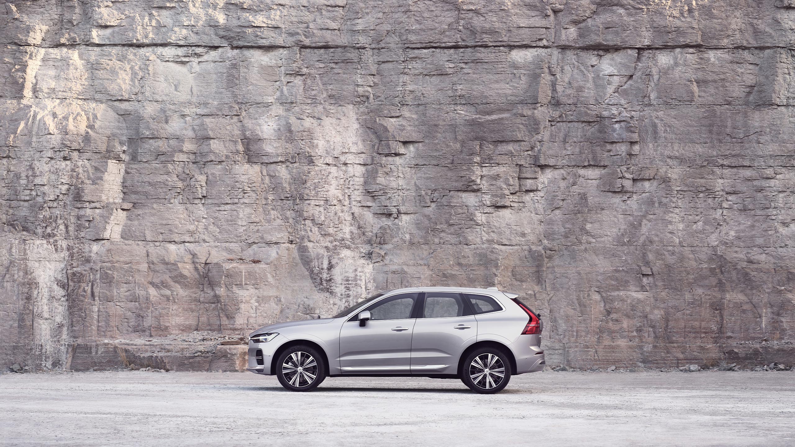 A Volvo XC60 standing still in front of a rock wall.