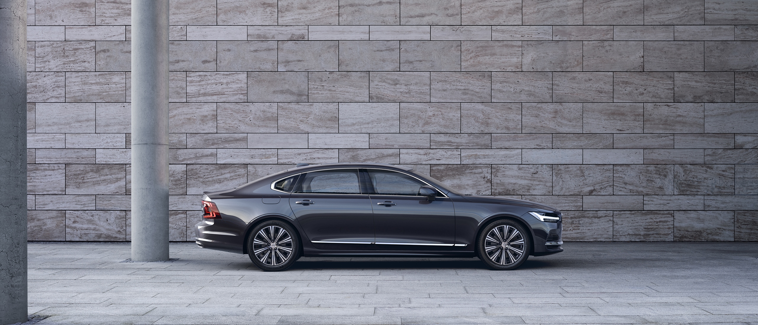 Volvo S90 seen from side parked in front of gray concrete wall.