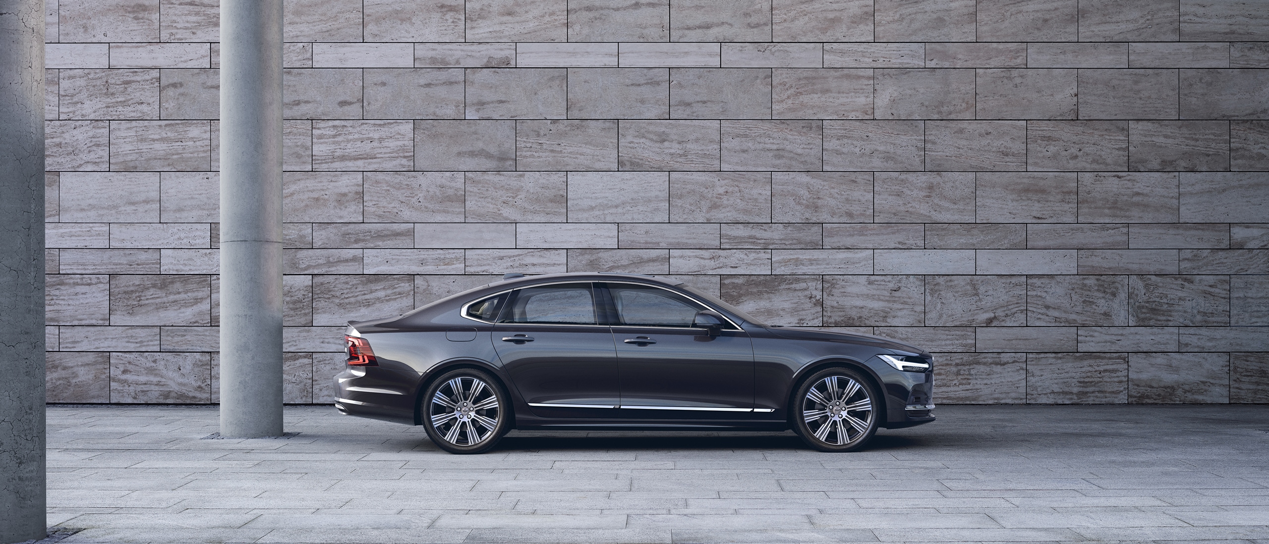 Volvo S90 seen from side parked in front of grey concrete wall.