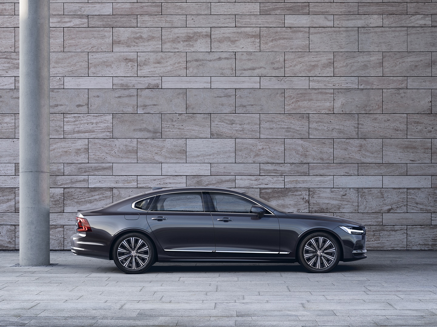 Volvo S90 seen from side parked in front of grey concrete wall.