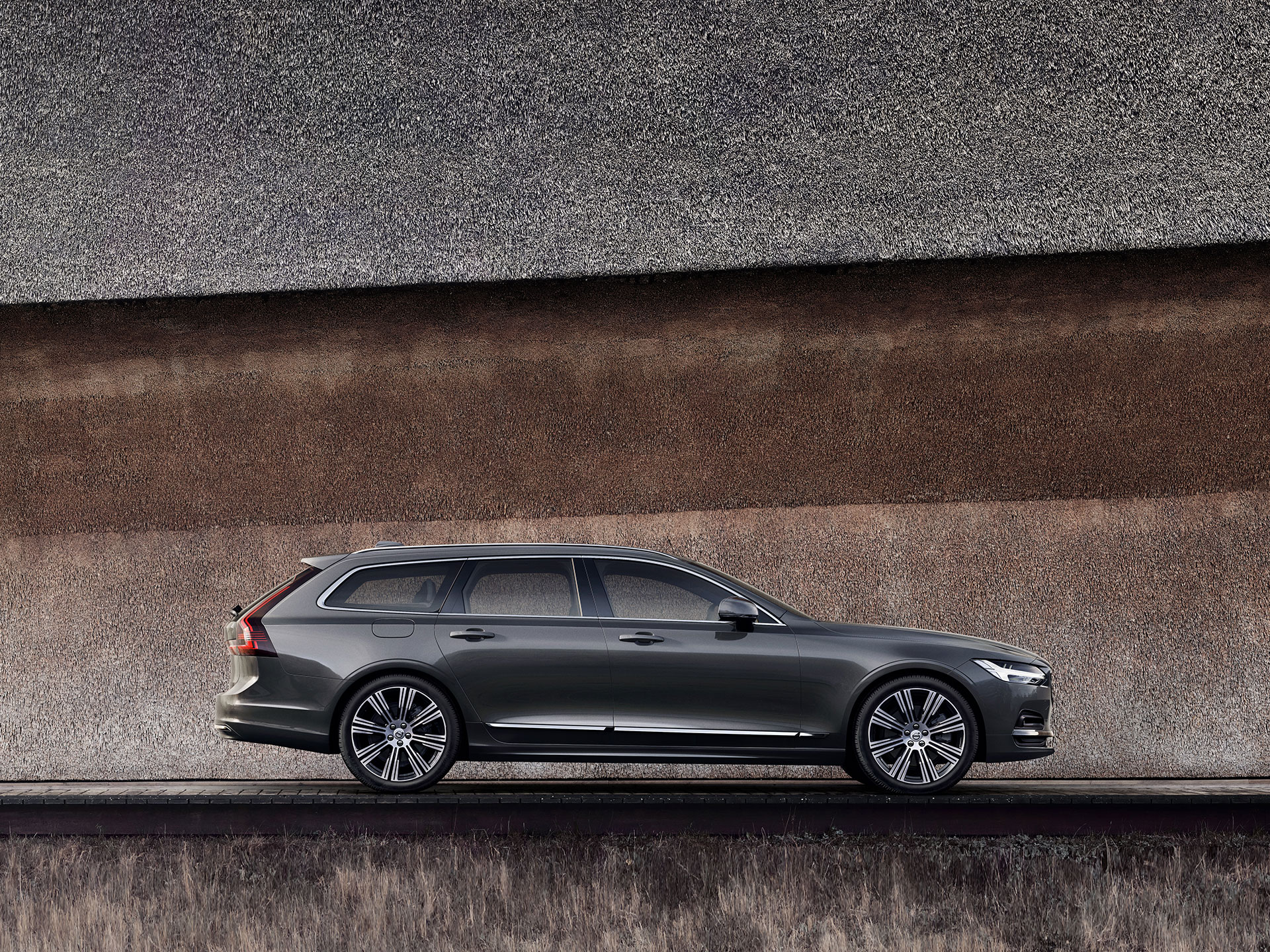 Una Volvo V90 grigio scuro parcheggiata contro un muro.