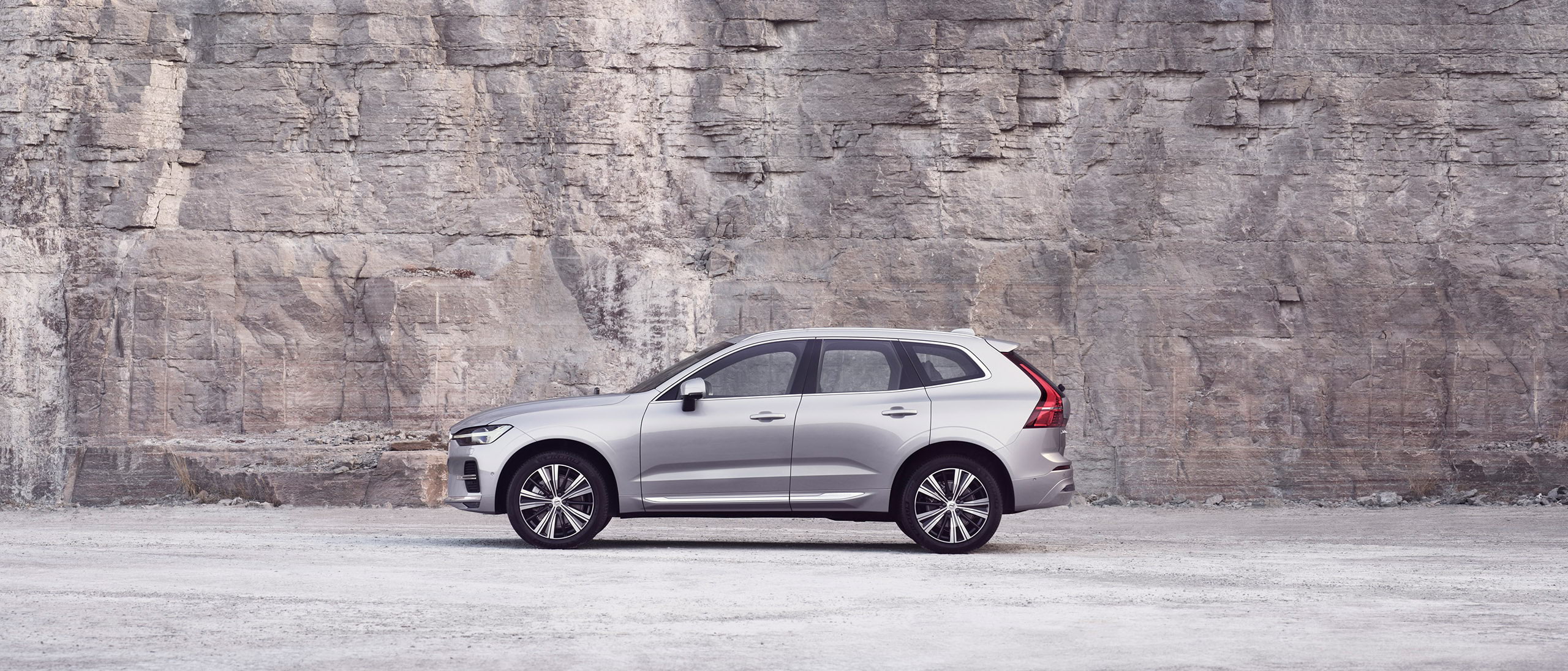 Un Volvo XC60 argintiu staționând în fața unui zid de piatră.