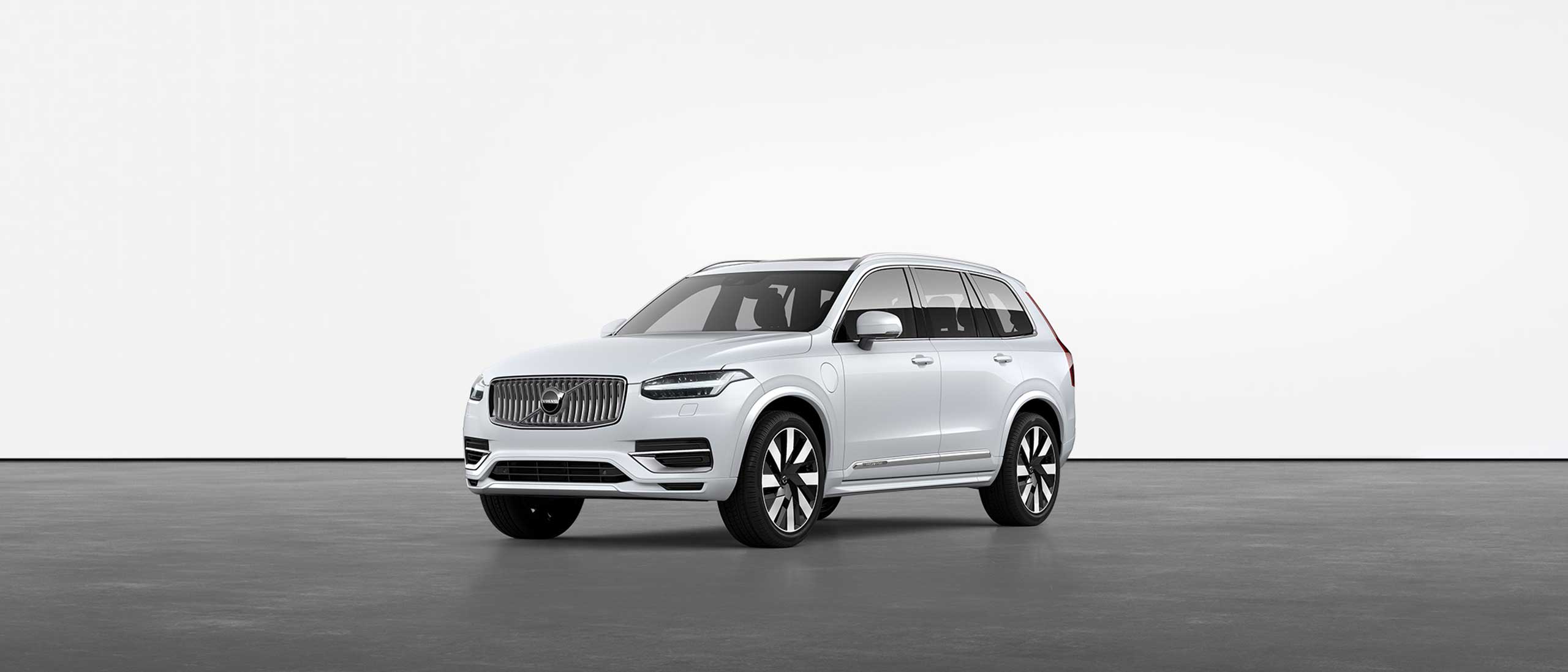 A white Volvo XC90 Recharge plug-in hybrid SUV standing still on grey floor in a studio.