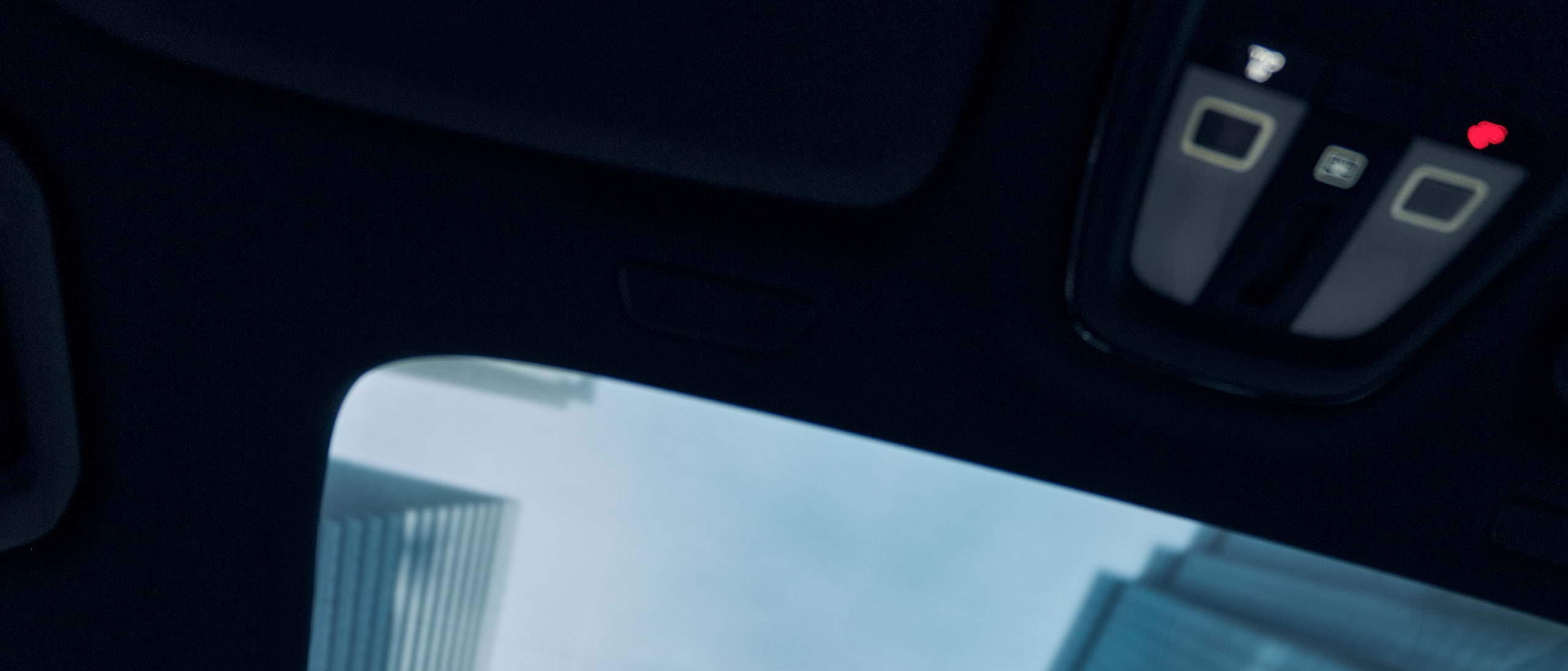 Skyscrapers are just visible through the panoramic roof of a moving Volvo car.