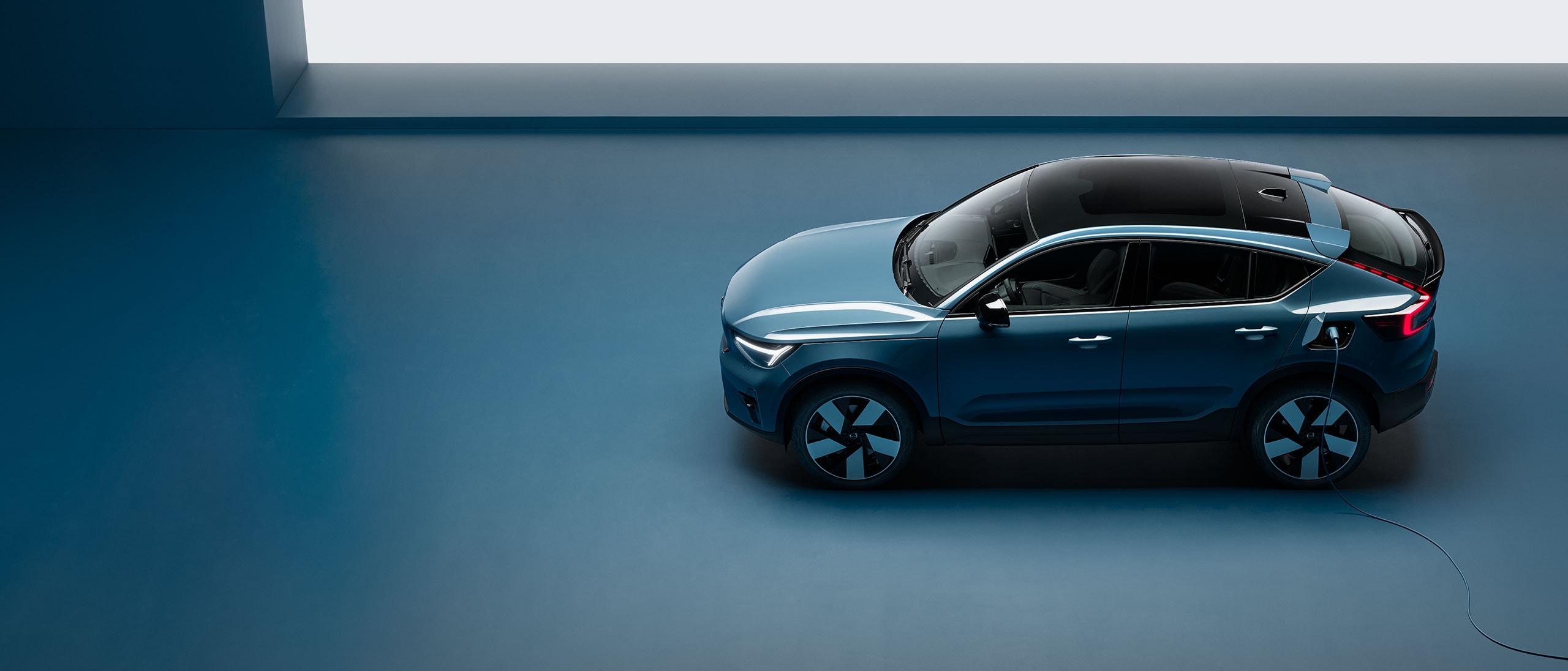 O mașină electrică Volvo încărcându-se cu un cablu de încărcare, într-un decor interior.