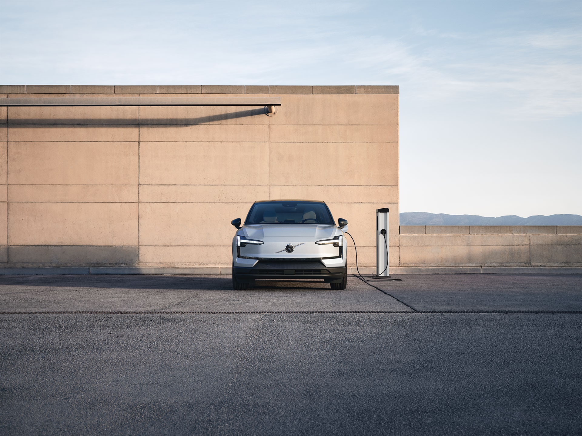 O mașină electrică Volvo încărcându-se la o stație de încărcare, într-un decor în aer liber.