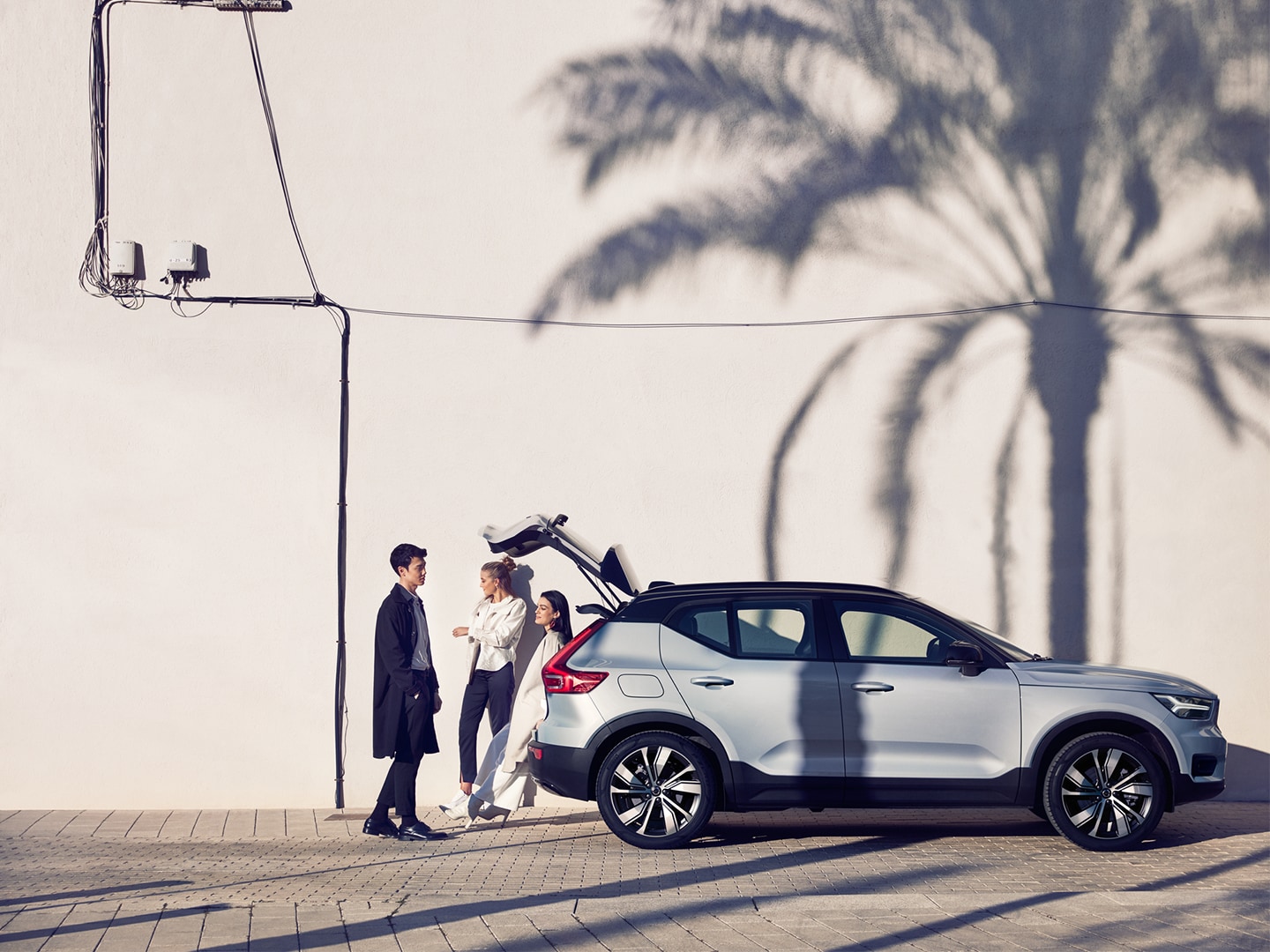 Three people gathered around open trunk of silver XC40 Recharge pure electric with black contrast roof. 