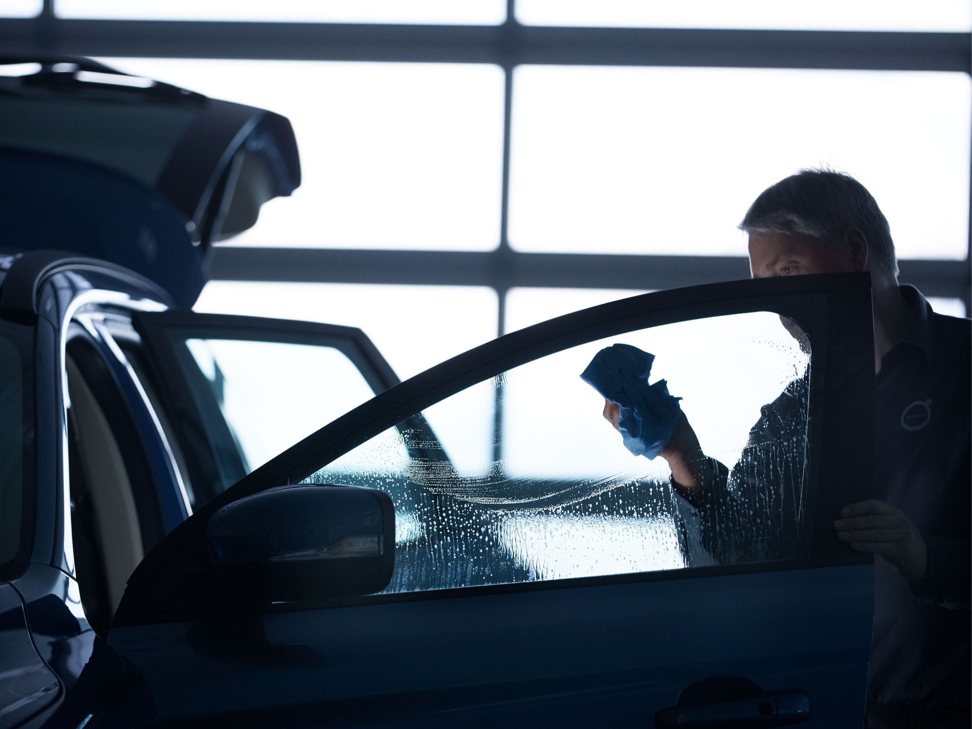 Una persona lavando el vidrio de la puerta de un vehículo.