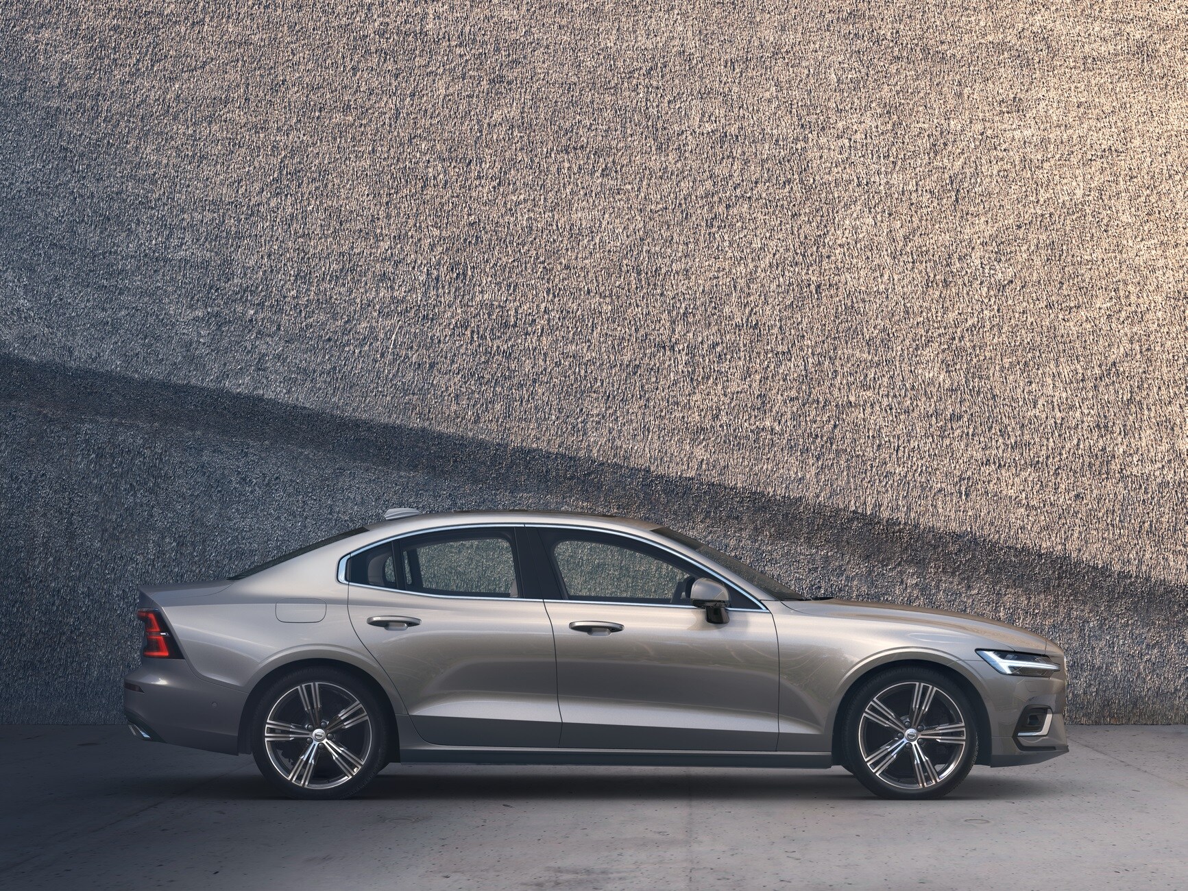 A Volvo Sedan Recharge parked outside in front of a big wall