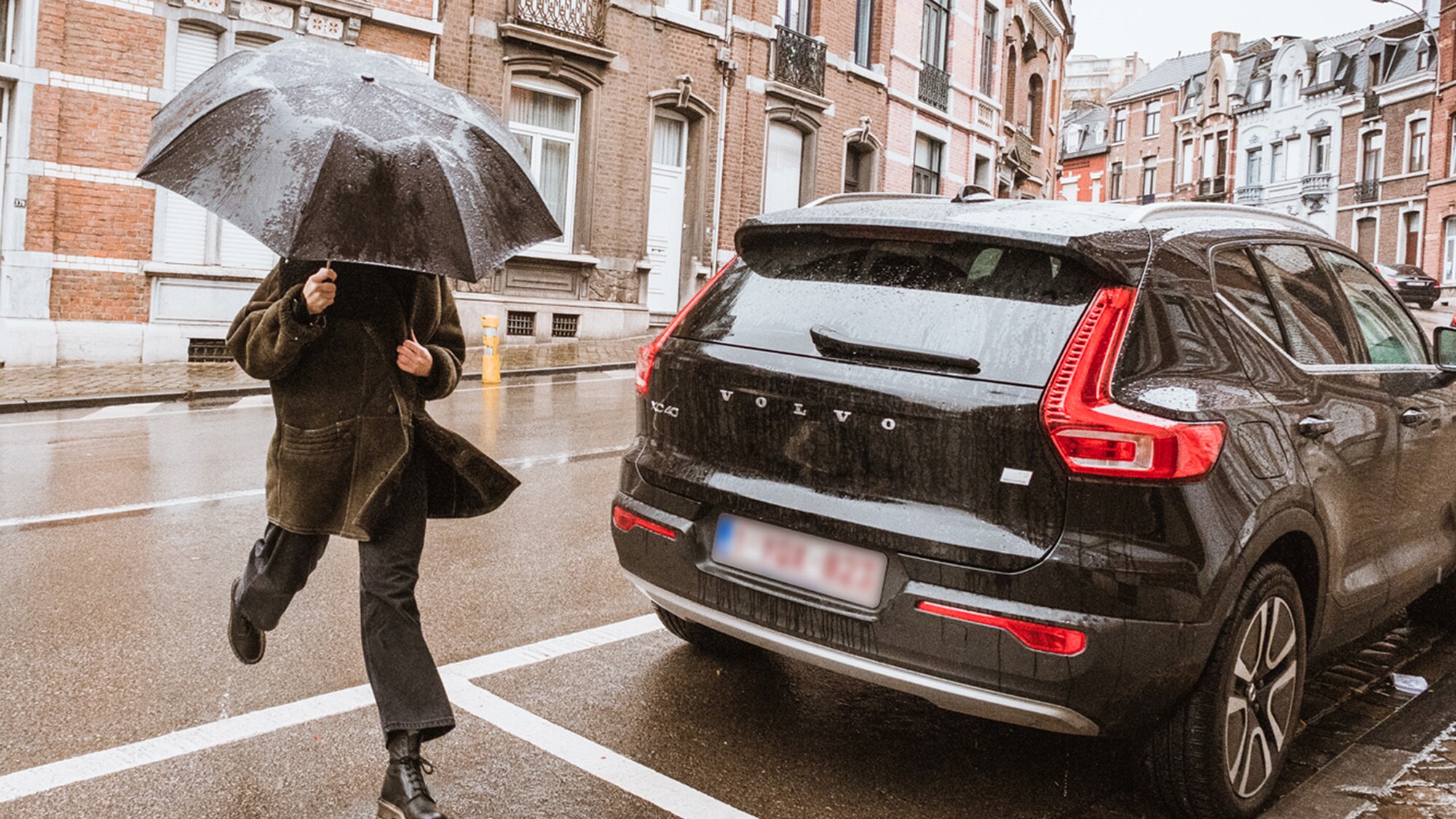 Een vrouw onder een paraplu loopt achter een Volvo XC40.