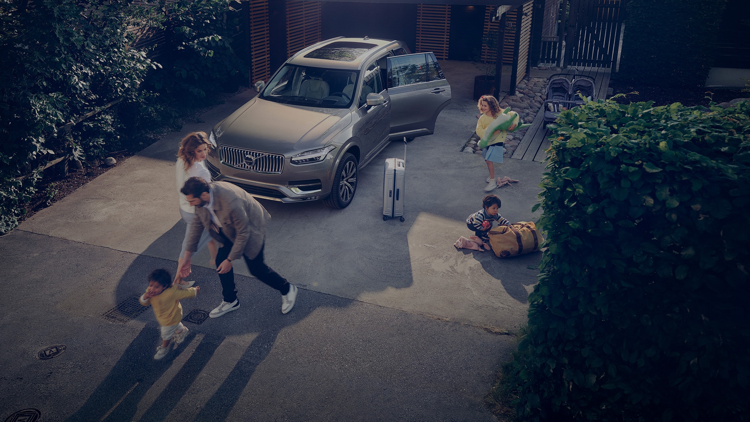 Une famille joue devant une Volvo XC60 avec la porte ouverte dans l'allée de leur maison.