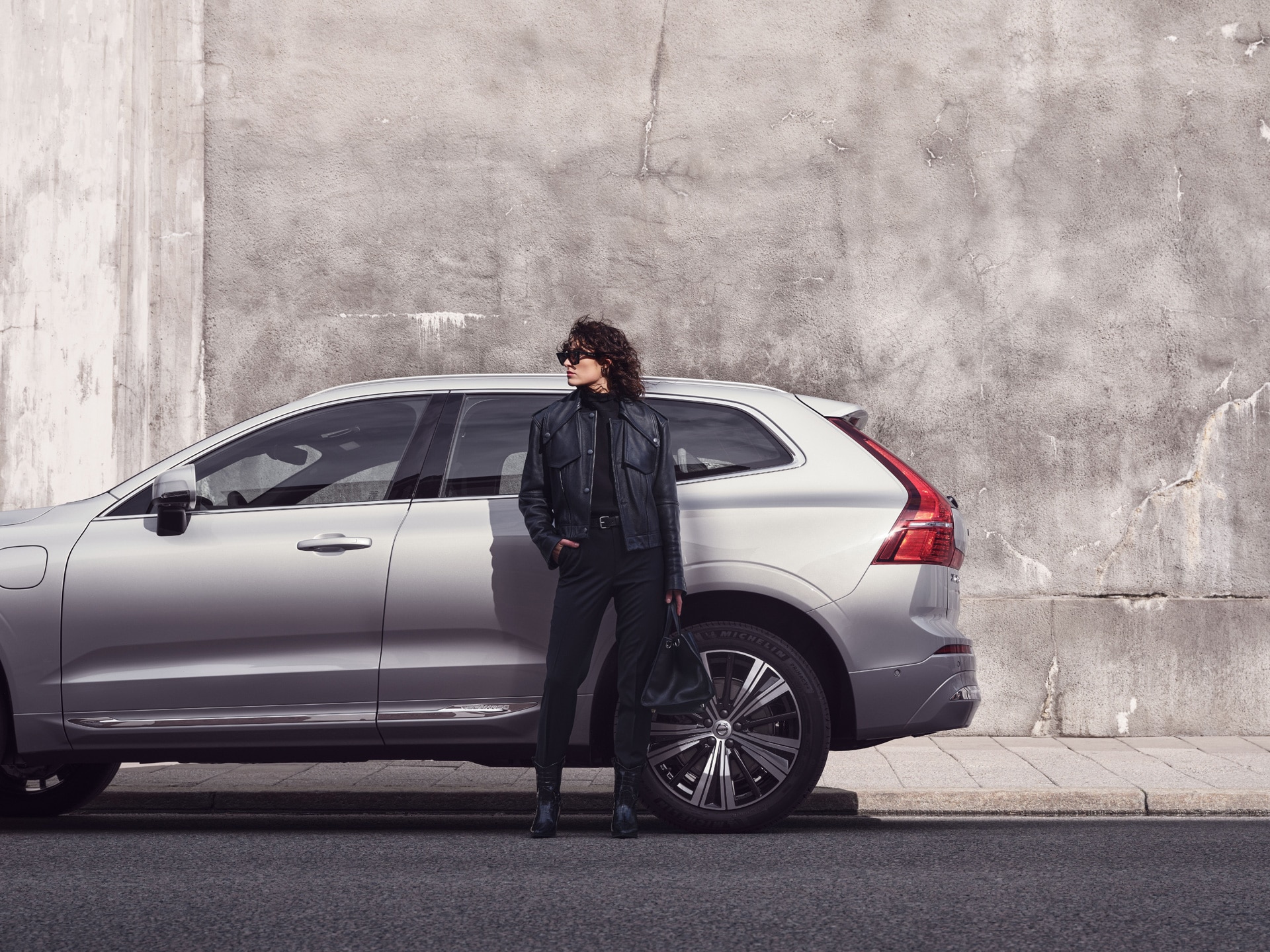 Una mujer recargada sobre el costado de un Volvo XC90 estacionado.