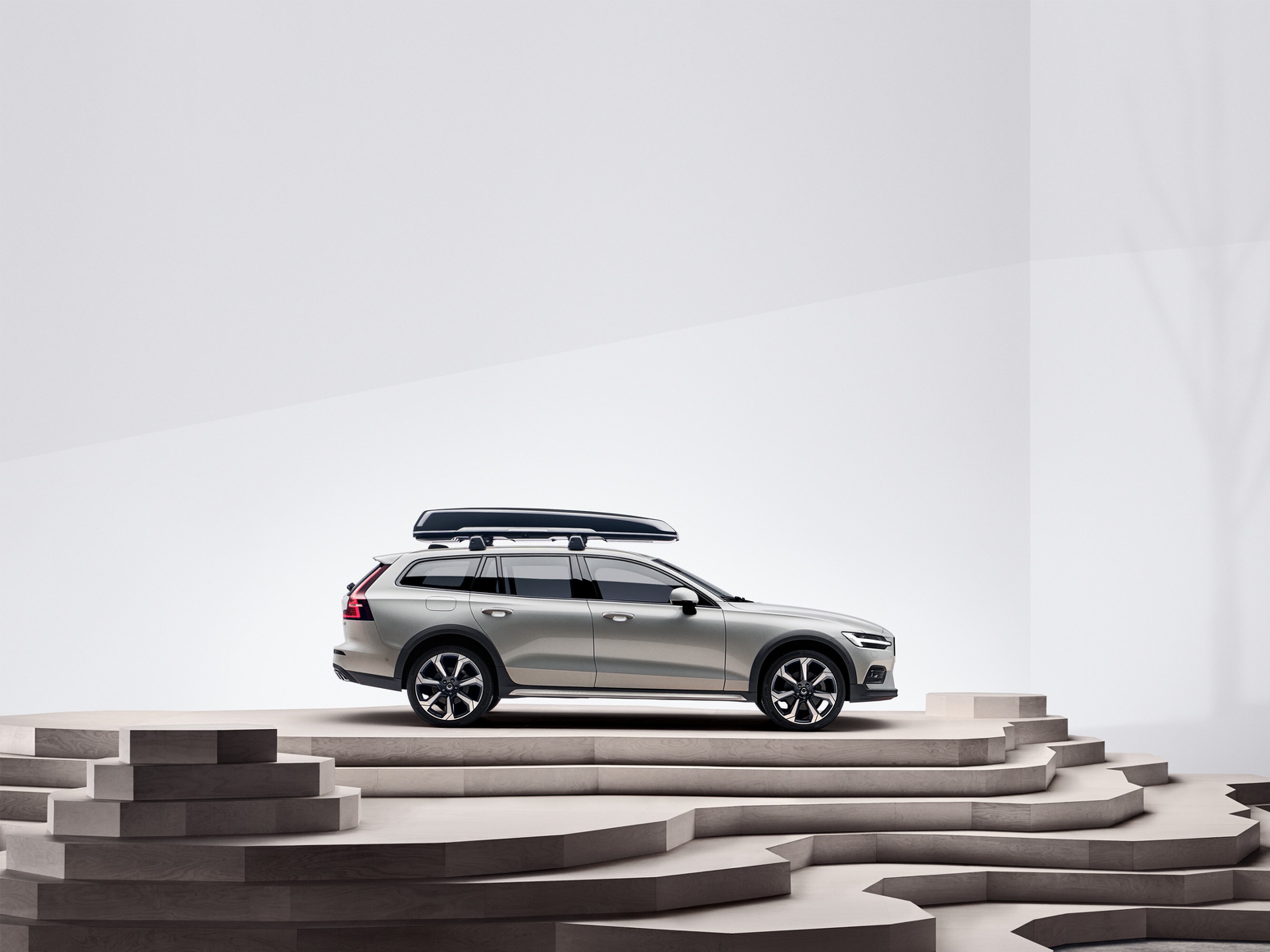 A beige Volvo V60 Cross Country with a roof box is parked on top of a staircase