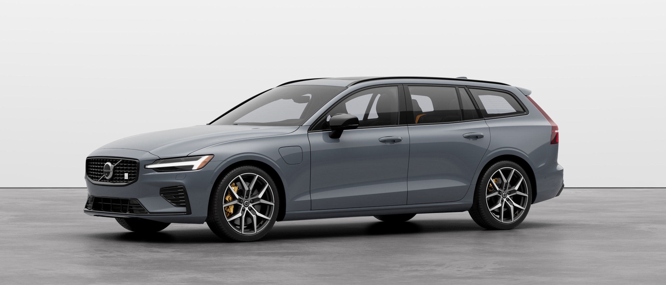 A white Volvo V60 Recharge plug-in hybrid SUV standing still on grey floor in a studio.