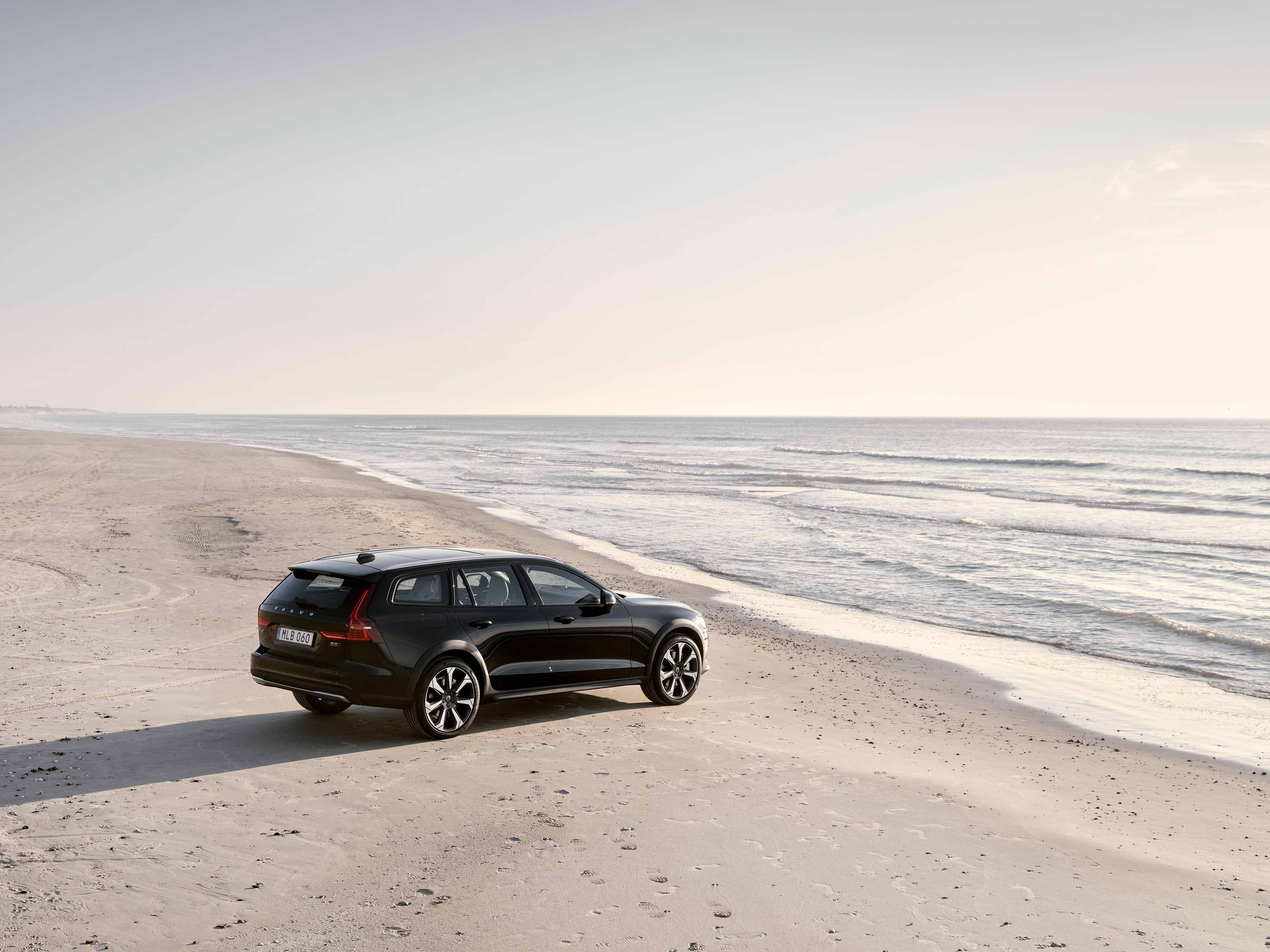 Black Volvo V60 CC parked on a beach by the sea.