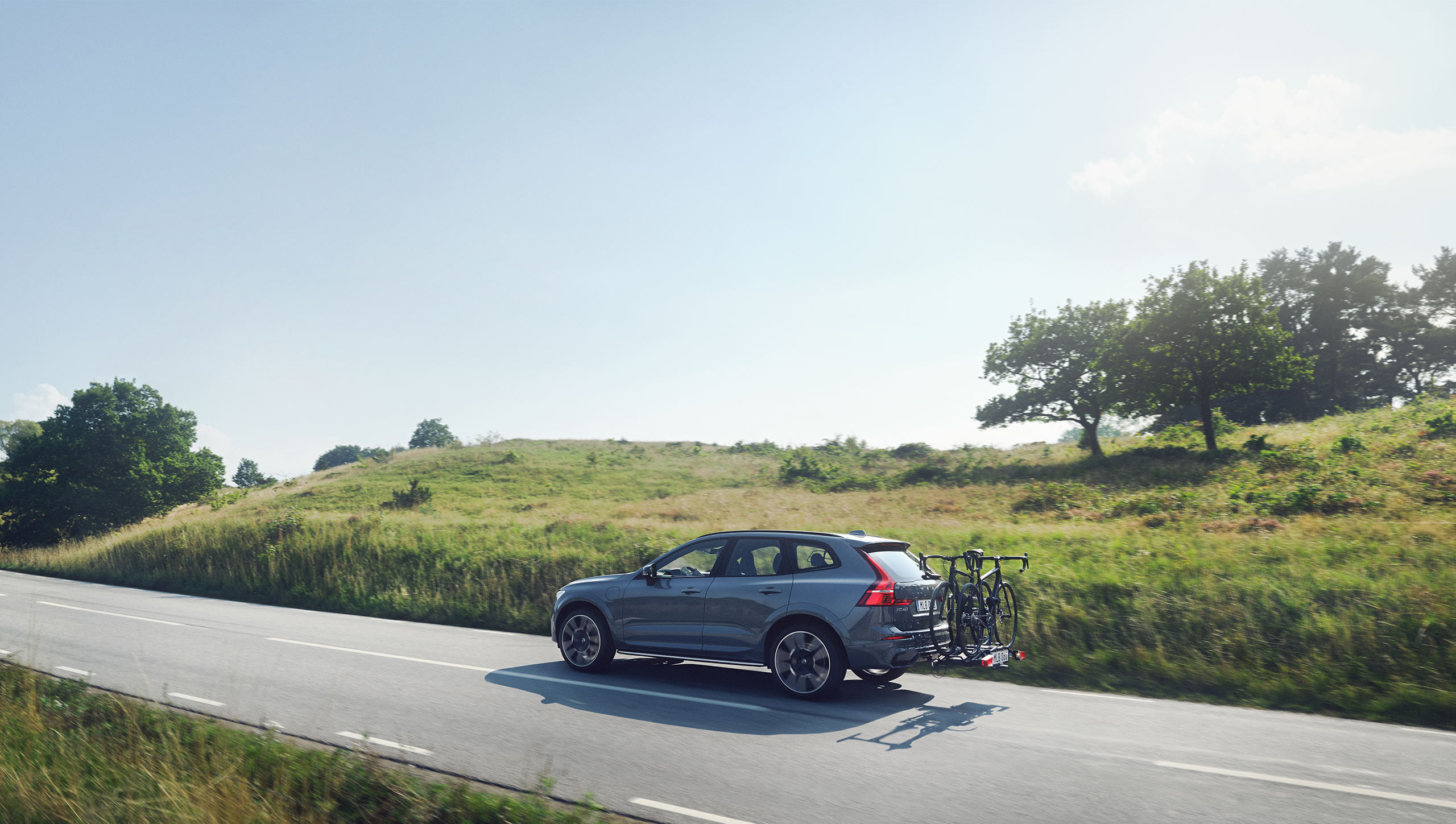 Thunder Grey Volvo XC60 Recharge driving between green fields on a sunny weather.