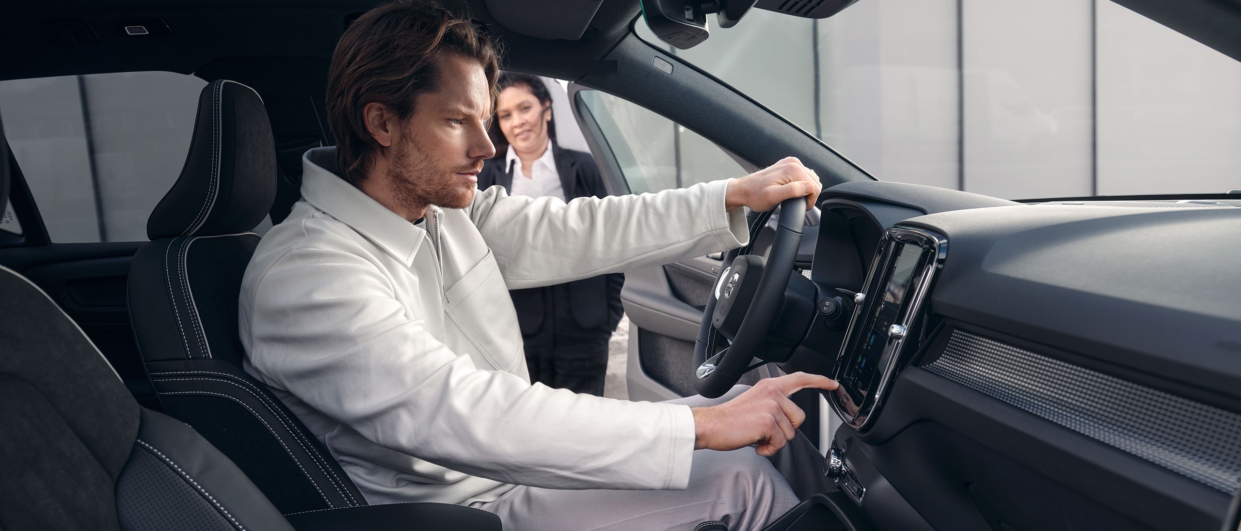 Mies istuu Volvo XC40 auton kuljettajan paikalla ja tutkii kojelaudan näyttöä.