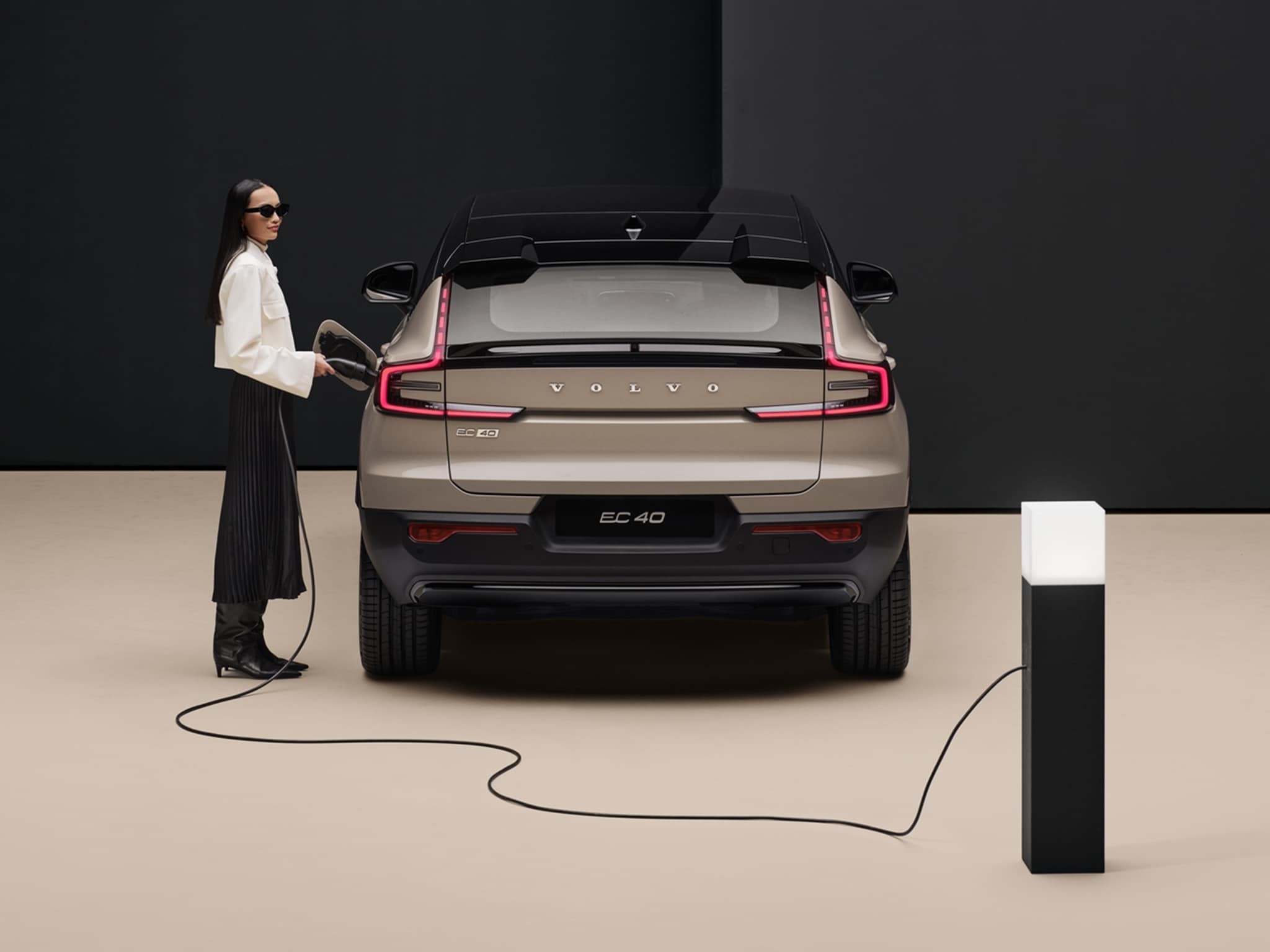 Nainen pitää kiinni Sand Dune -väriseen Volvo EC40 autoon kytketystä lataupistokkeesta. 