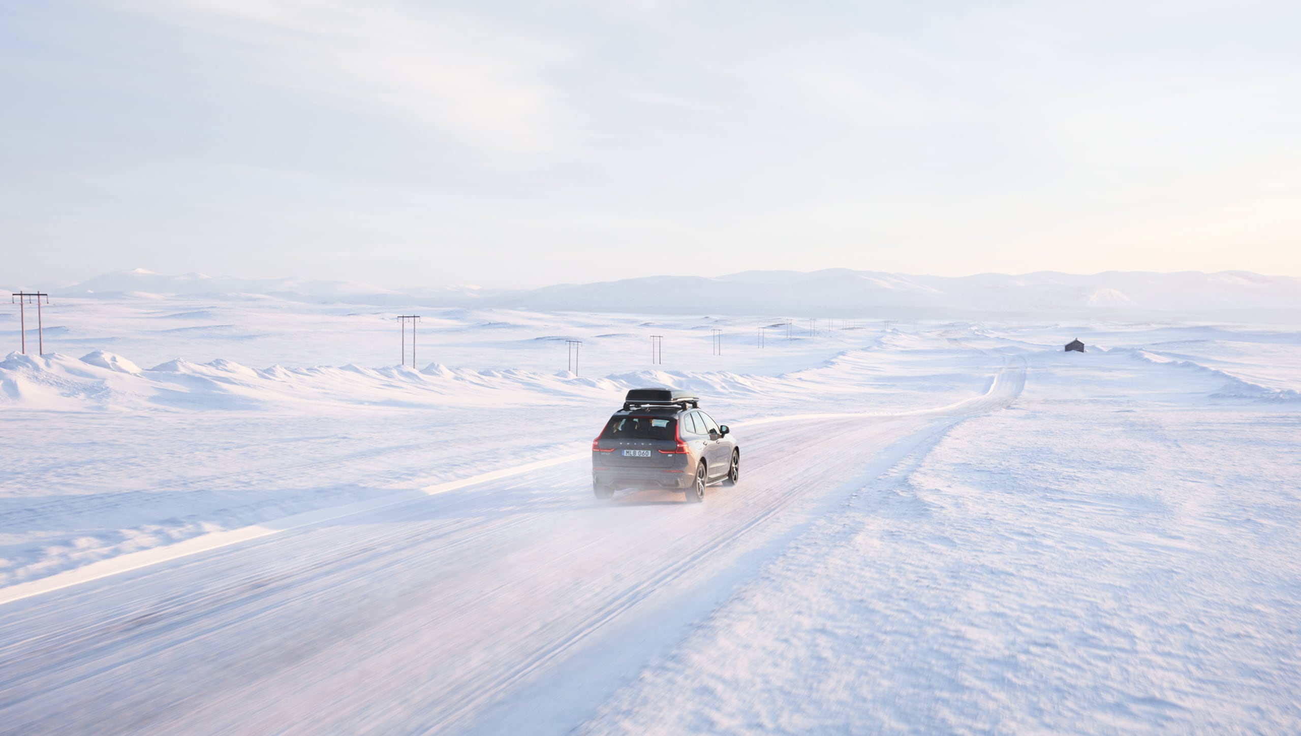 Thunder Grey -värinen Volvo XC60 ajaa lumisella tiellä talvimaisemassa. 