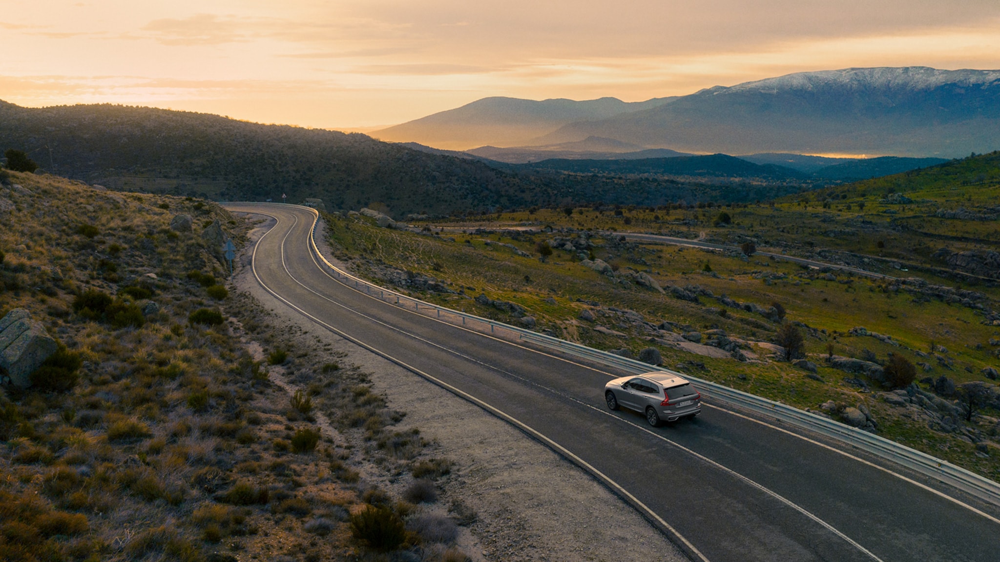 Silver Dawn -värinen Volvo XC60 ajaa vuoristotiellä auringonlaskun aikaan.