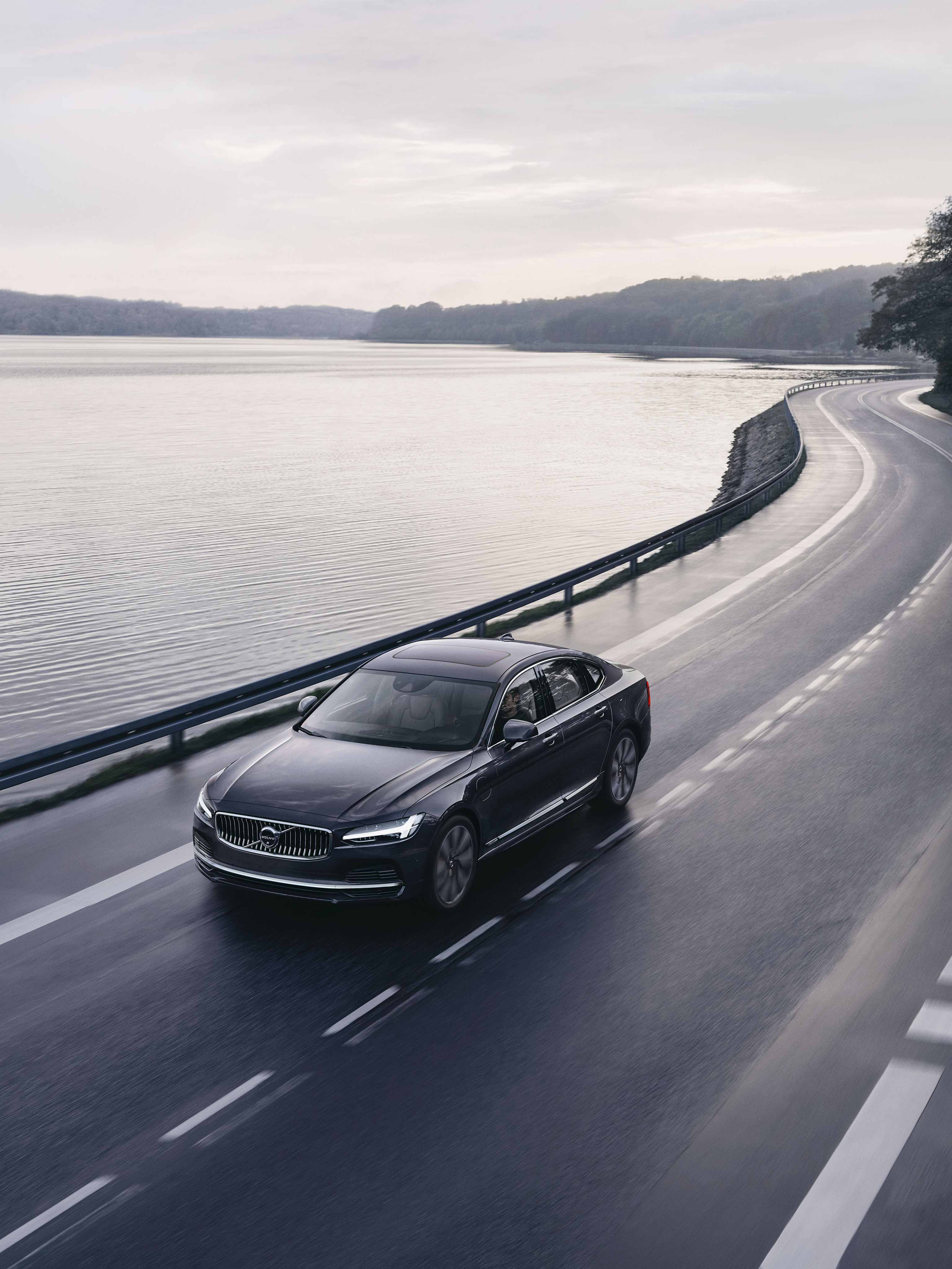 lack Volvo S90 driving by road by the lake.