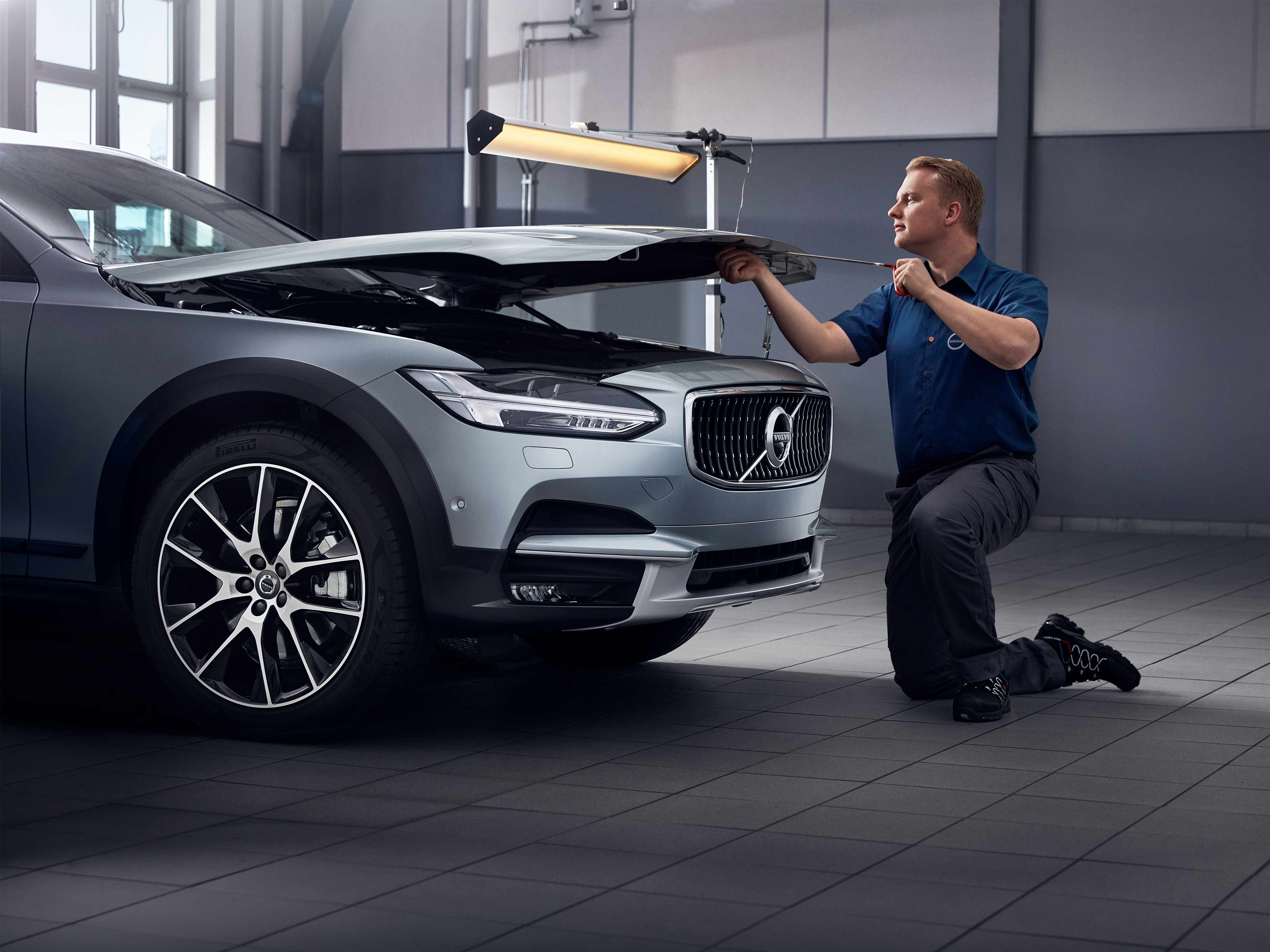 Man repairing a Volvo car with hood open.