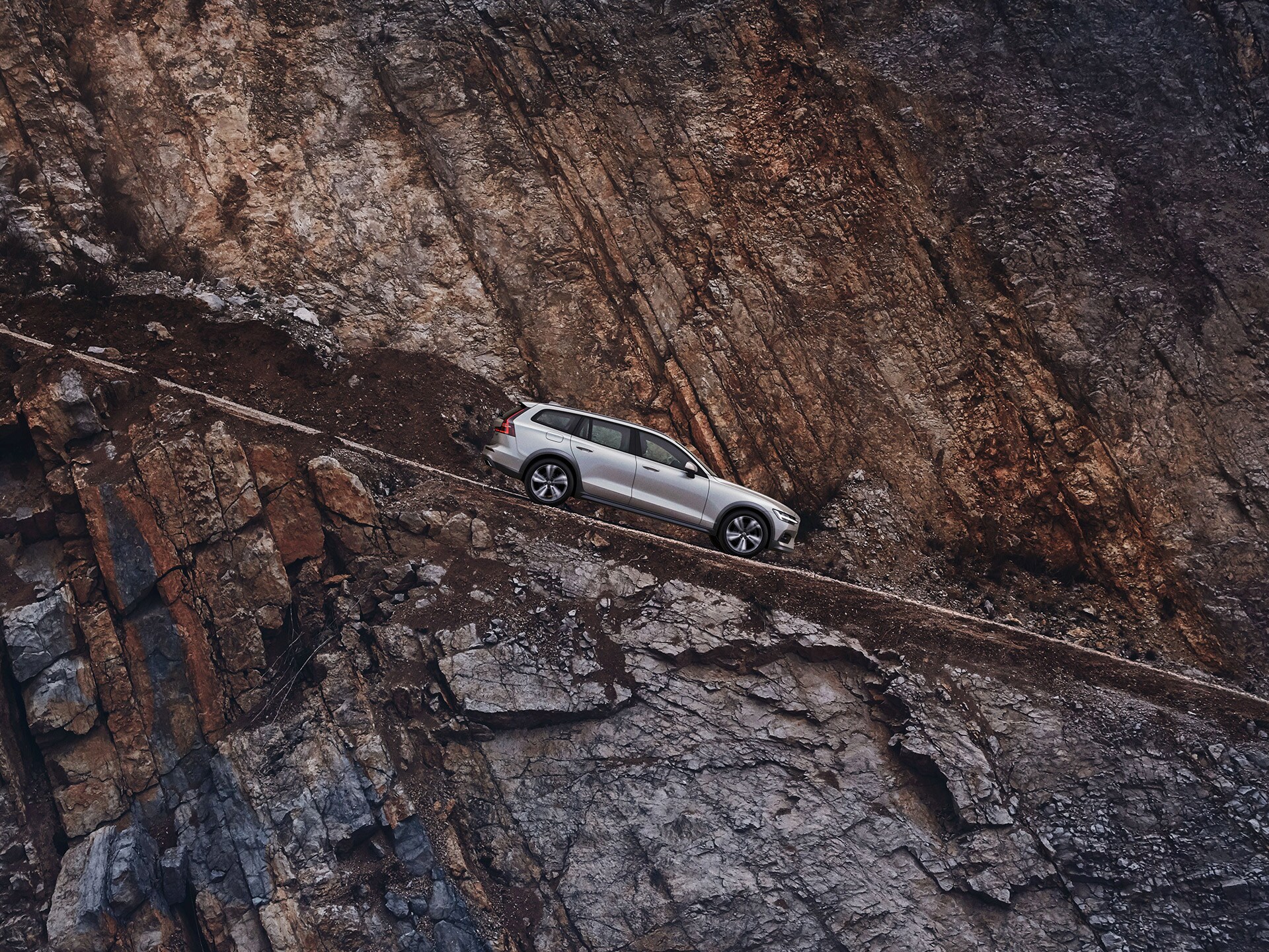 Volvo V60 Cross Country gris clair descendant une côte à flanc de falaise en pierre rouge