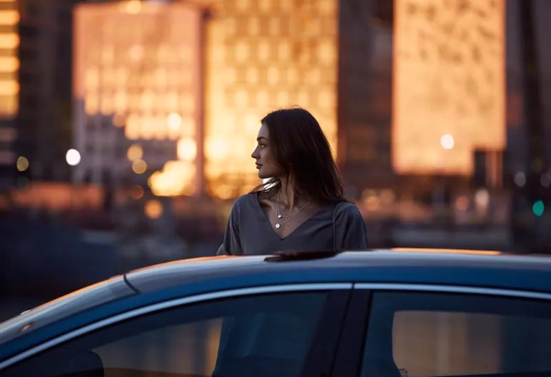 Femme debout derrière un Volvo Bleu