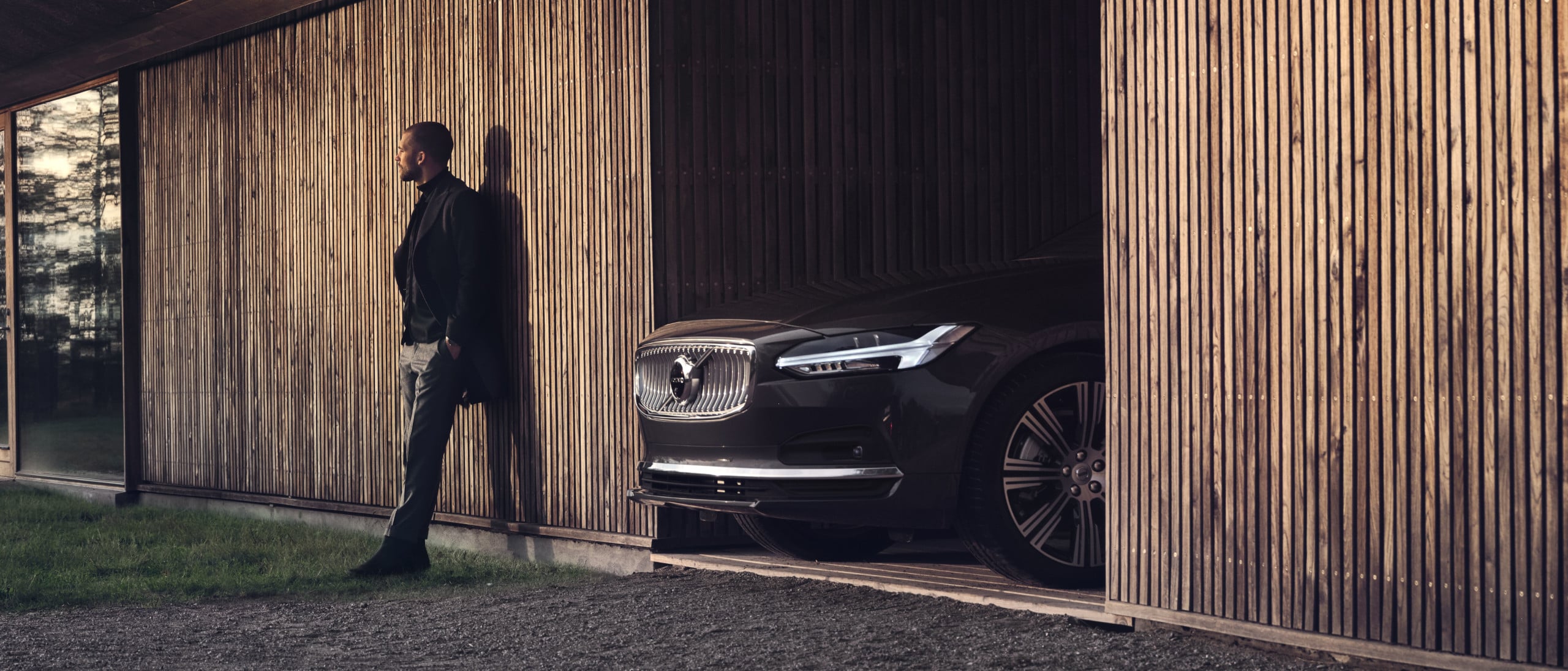Volvo - Talent steht vor einer Holzwand mit einem Volvo daneben - Frontseitenschuss