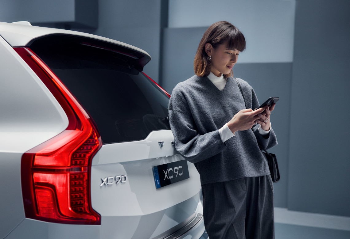 Eine Frau lehnt mit einem Handy in der Hand an einem Volvo Fahrzeug