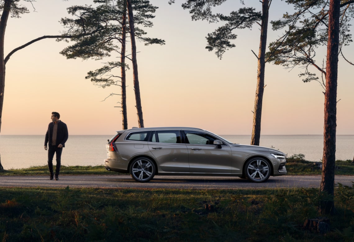 Person steht hinter einem Volvo V60 bei Sonnenuntergang am Meer