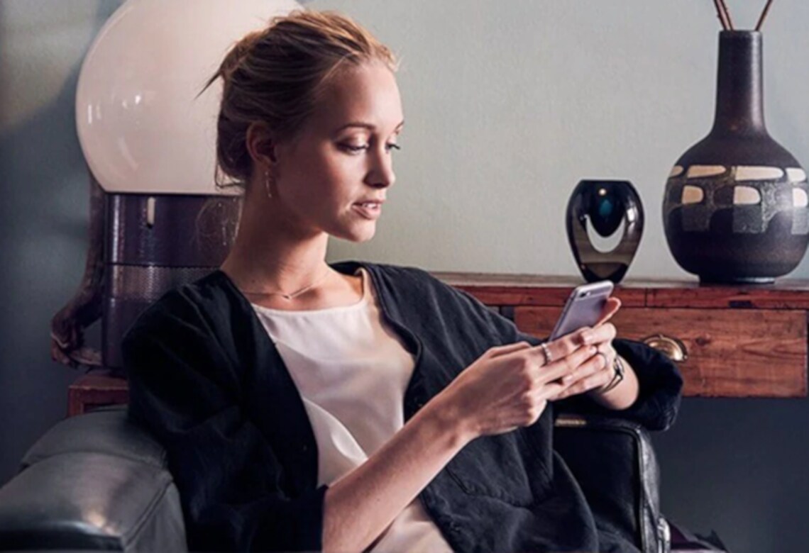 Frau sitzt auf Couch und guckt auf ihr Smartphone