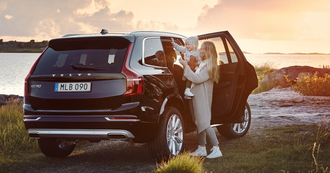 Frau hat ein Kind auf dem Arm und steht an der geöffneten Beifahrertür eines Volvo XC90