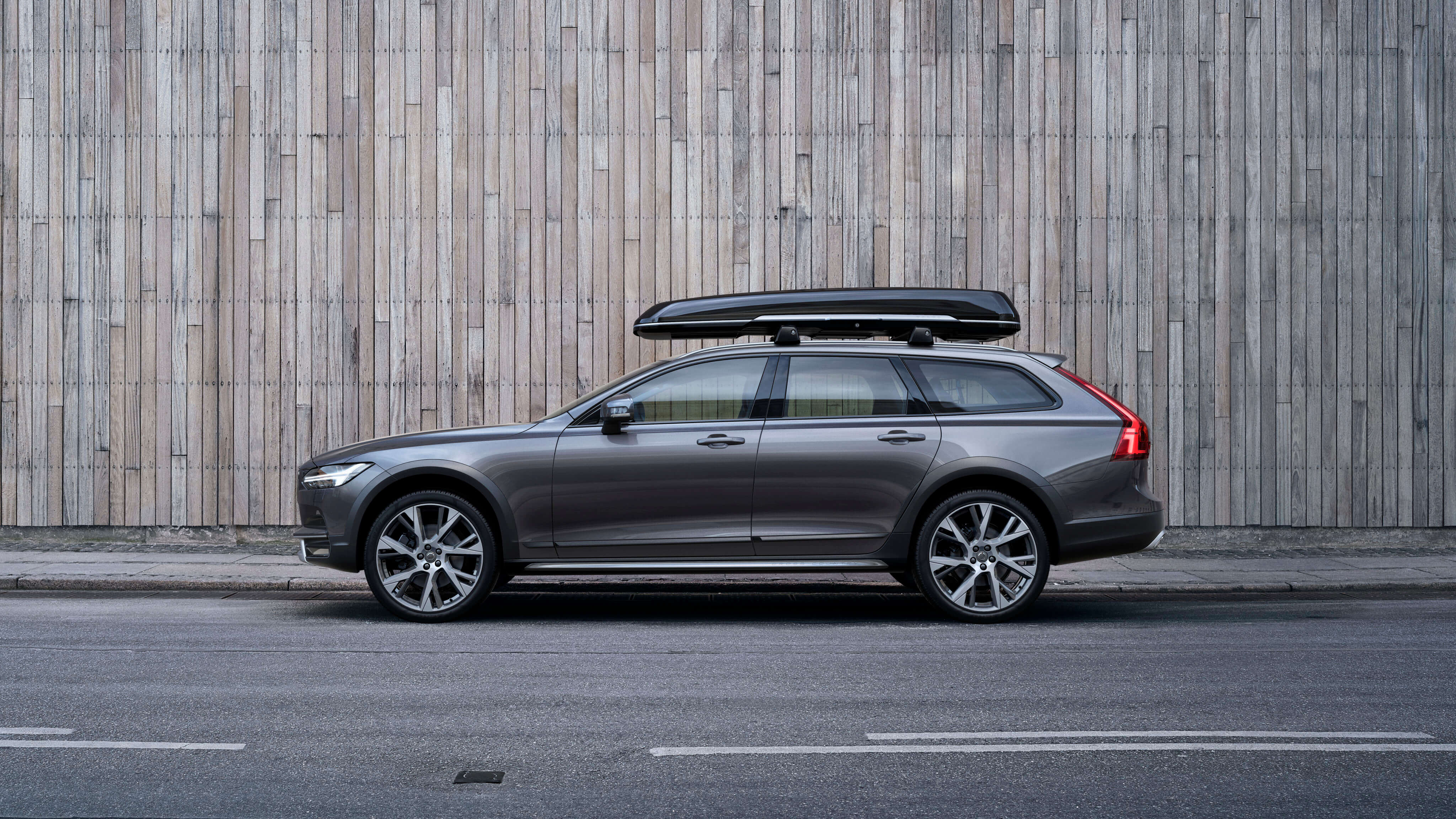 Volvo V90 CROSS COUNTRY mit Dachbox steht vor einer Wand - Seitenschuss