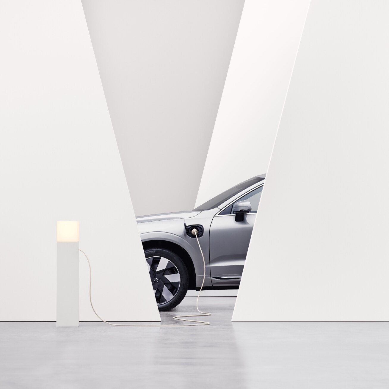 Vue partielle d'une Volvo d'un angle latéral, dans un environnement intérieur blanc, en charge à une borne de recharge